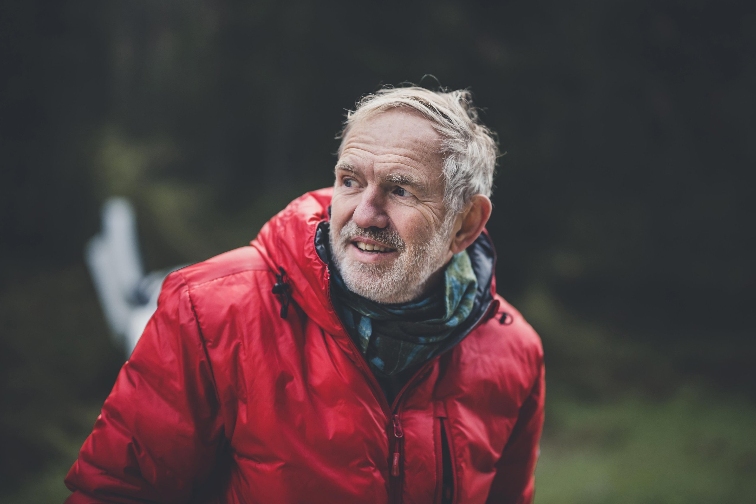 Anton Corbijn Photographs The Revuelto Like A Rock Star, And That'S Exactly Lamborghini'S Point 5 Close-up portrait of anton corbijn with grey beard wearing a red puffer jacket and patterned scarf, looking thoughtfully to the side in a forest setting