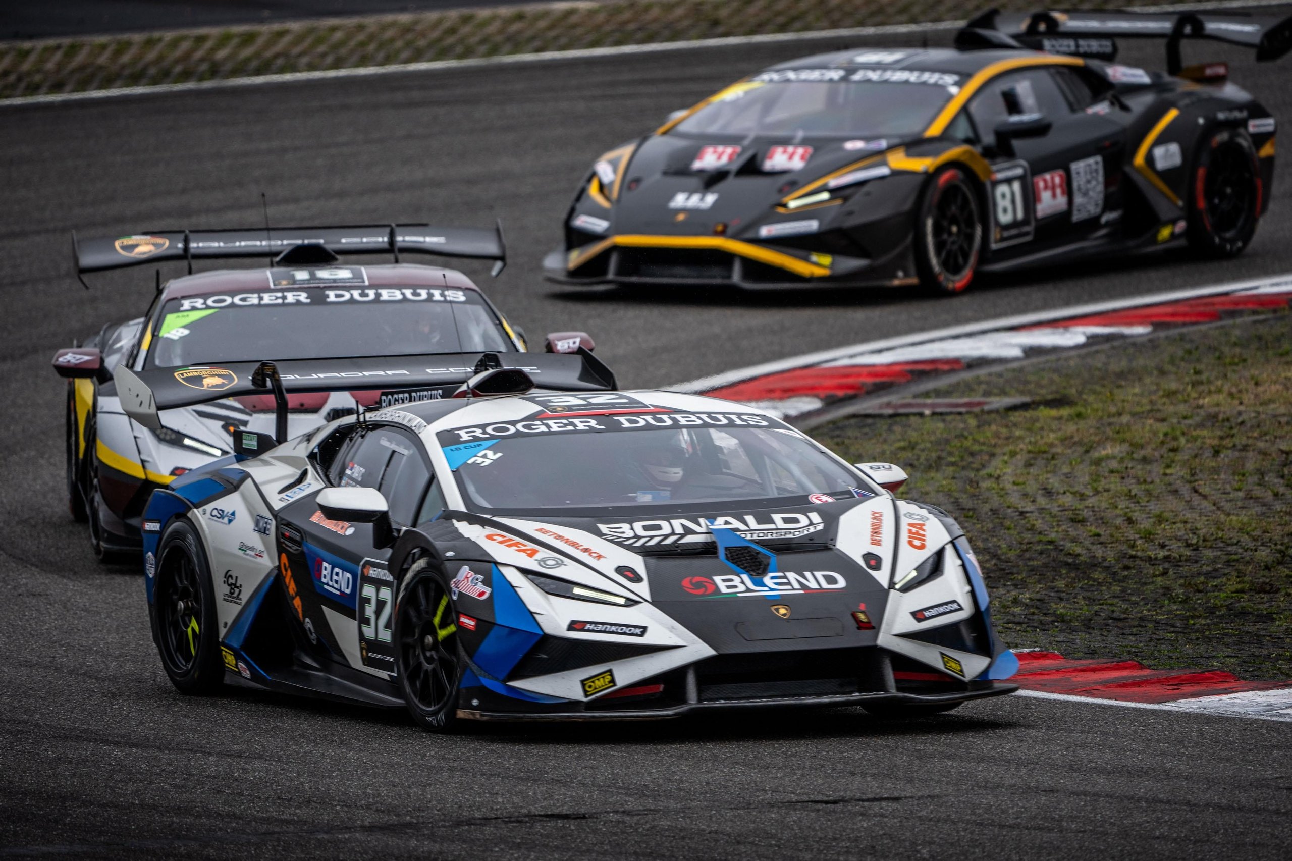 A 17-Year-Old Egyptian Just Rewrote The Record Books At Nürburgring'S Super Trofeo Europe Round 7 Two lamborghini huracán super trofeo evo2 race cars in white/blue and black/yellow liveries racing closely through a nürburgring corner