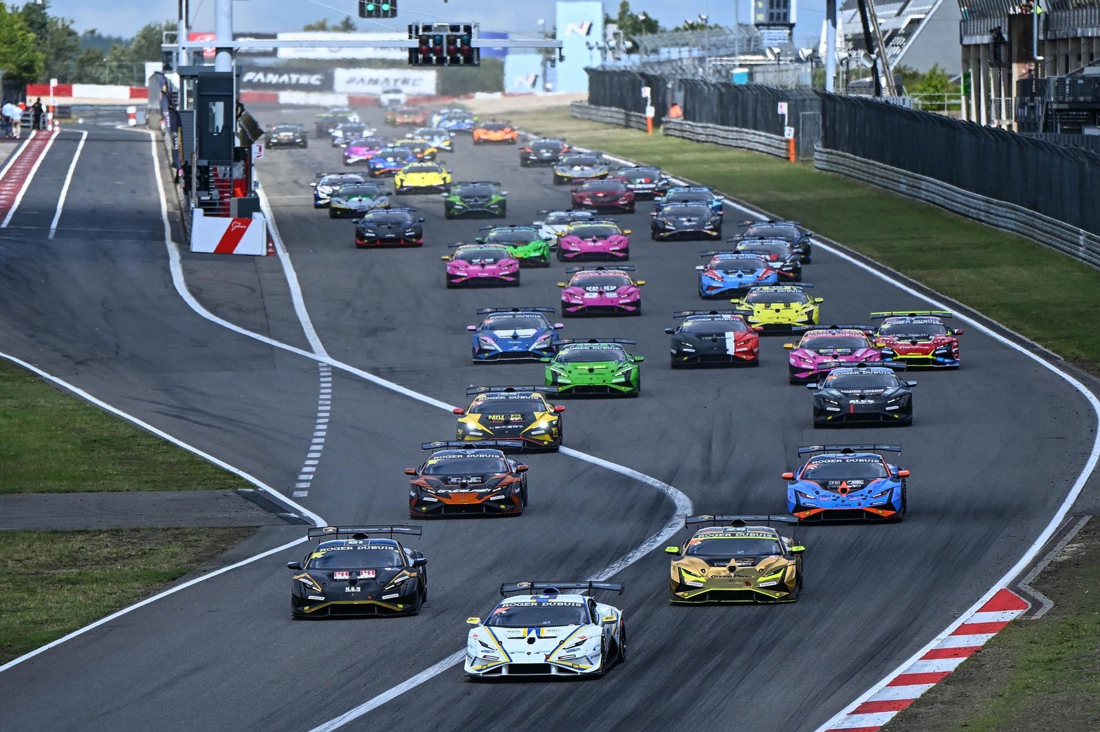 A full grid of Lamborghini Huracán Super Trofeo EVO2 race cars in diverse liveries navigating a turn during the Nürburgring round