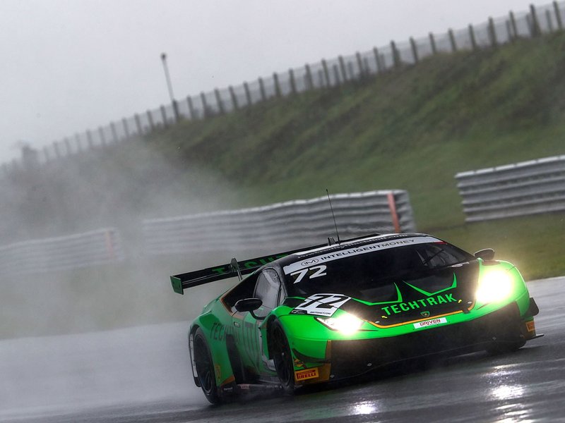 The #72 Barwell Lamborghini Huracán GT3 Evo cutting through spray on a wet Snetterton circuit with headlights blazing