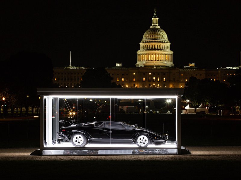 The Cannonball Run Lamborghini Countach LP 400 S displayed in an illuminated glass case on the National Mall with the US Capitol Building in the background at night