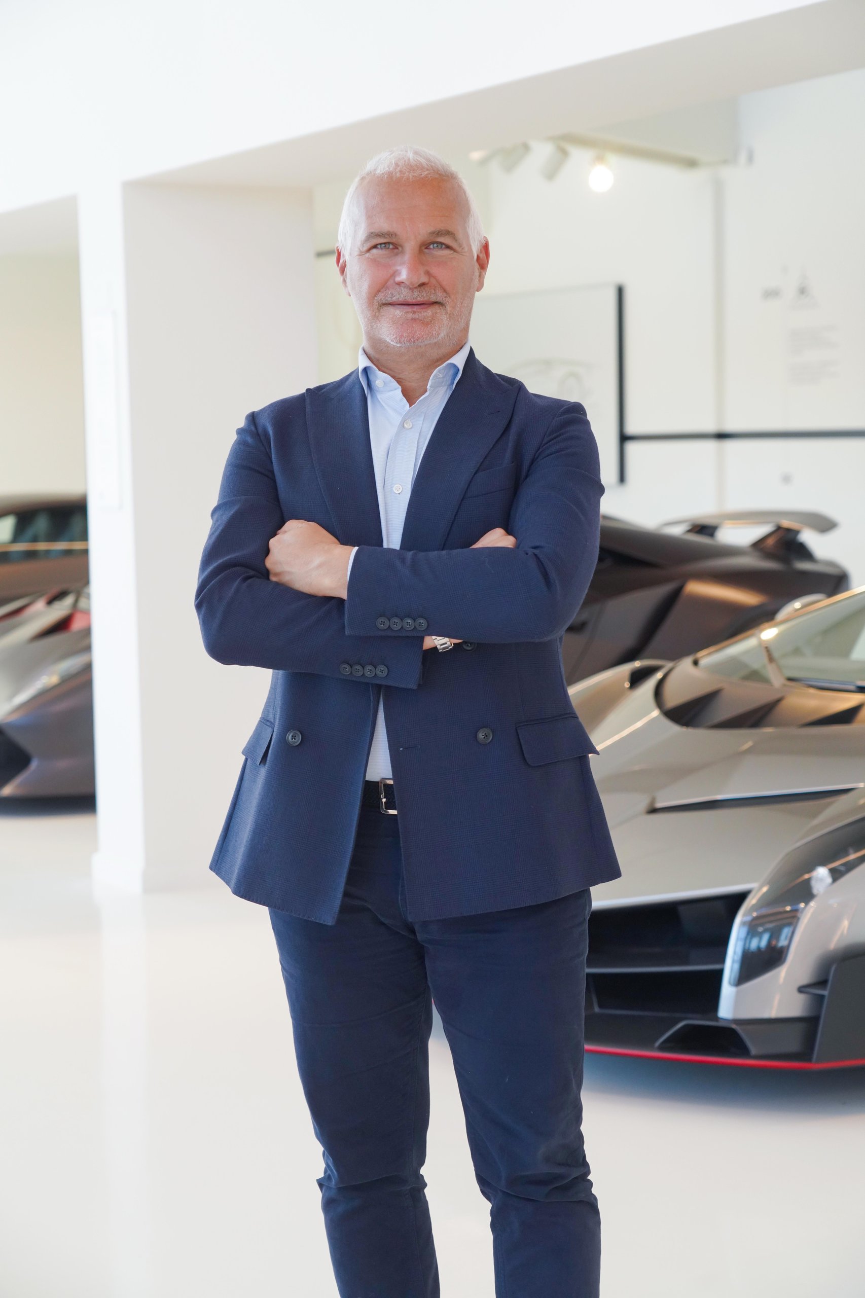 Christian mastro standing with crossed arms between two futuristic lamborghini limited-production models in a showroom
