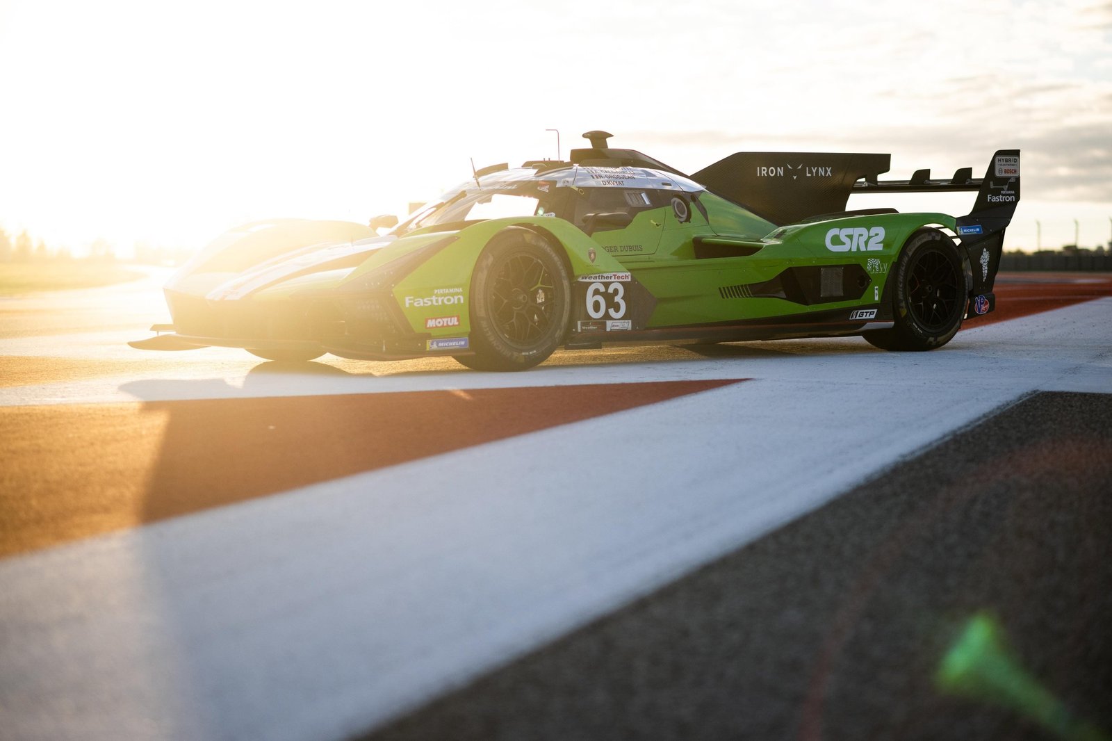 Green Lamborghini SC63 number 63 race car parked on track at sunrise showing aggressive front profile