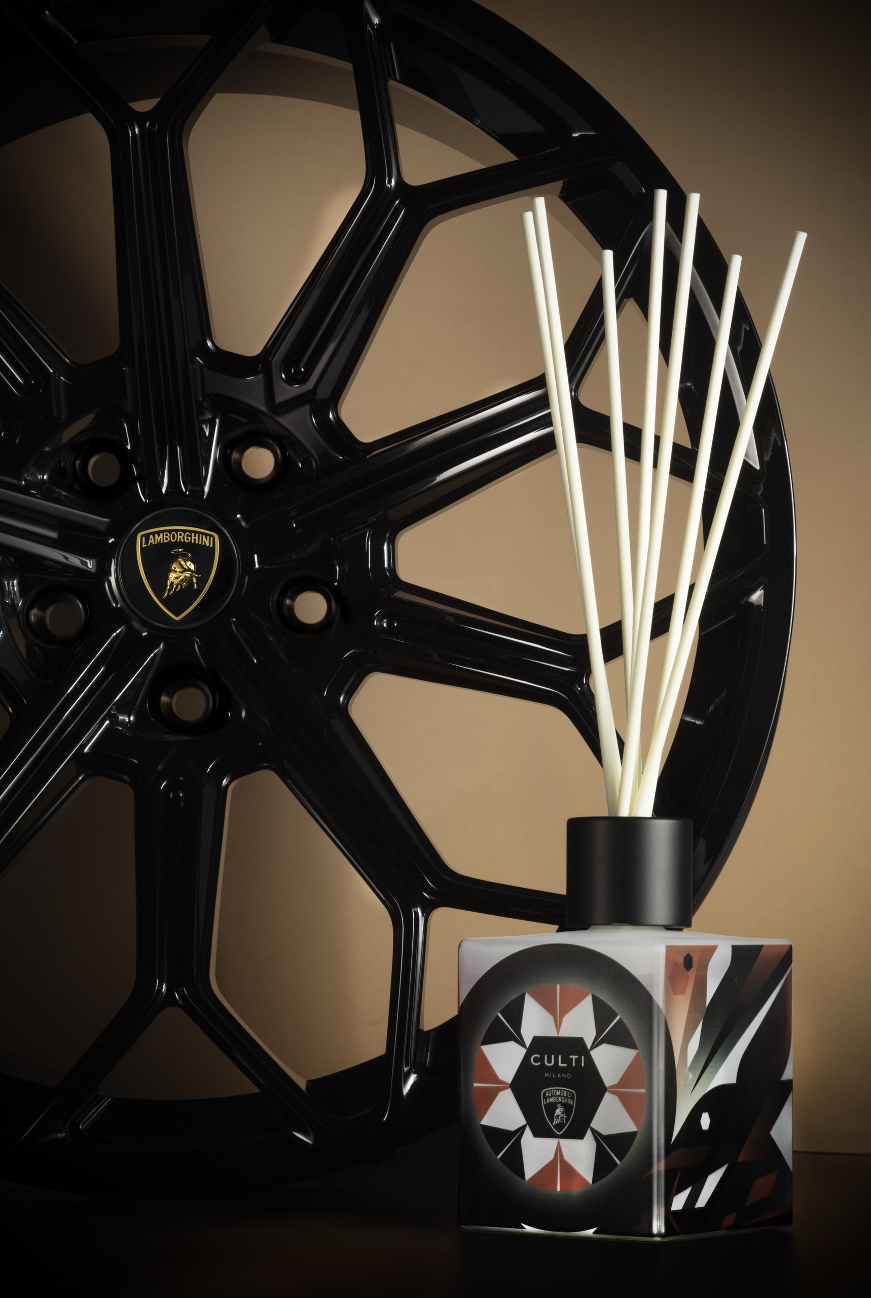 Culti milano for automobili lamborghini reed diffuser with geometric pattern positioned in front of a black lamborghini wheel with shield emblem