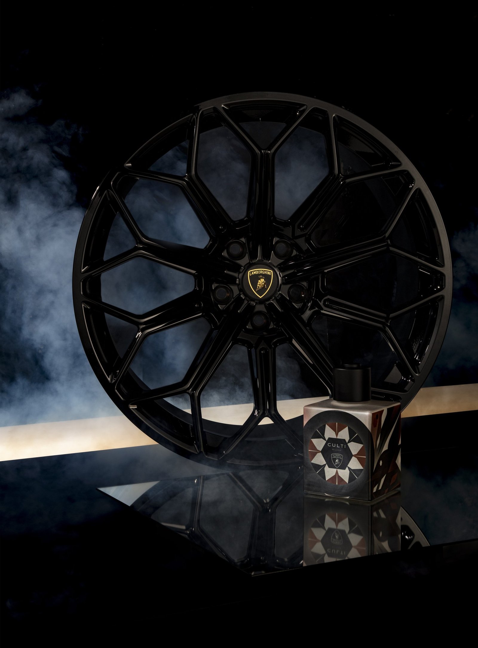 CULTI MILANO for Automobili Lamborghini perfume bottle placed beside a black Lamborghini wheel with dramatic smoke effects