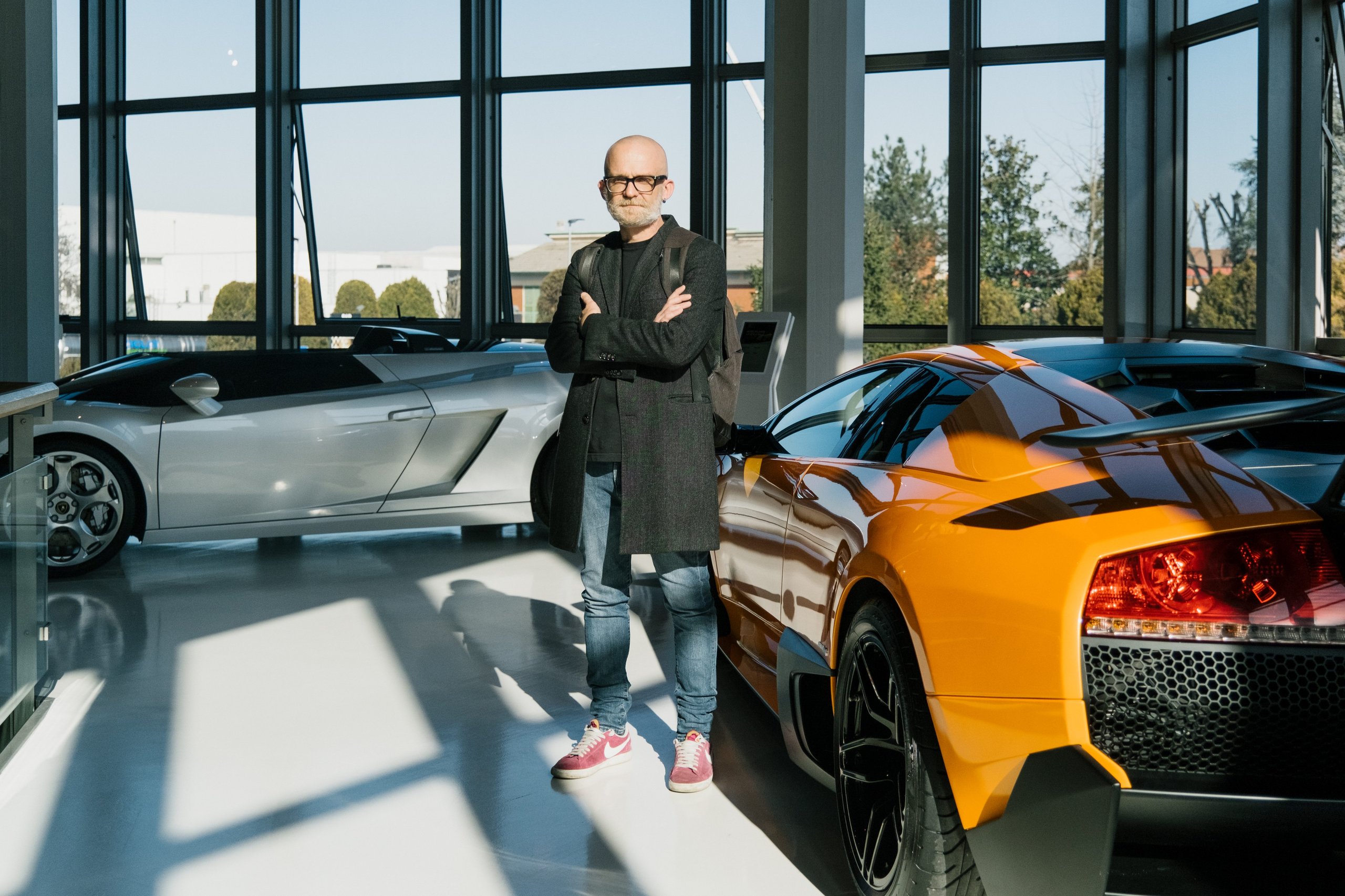 Francesco poroli standing between an orange lamborghini murciélago and a silver lamborghini gallardo in a bright showroom