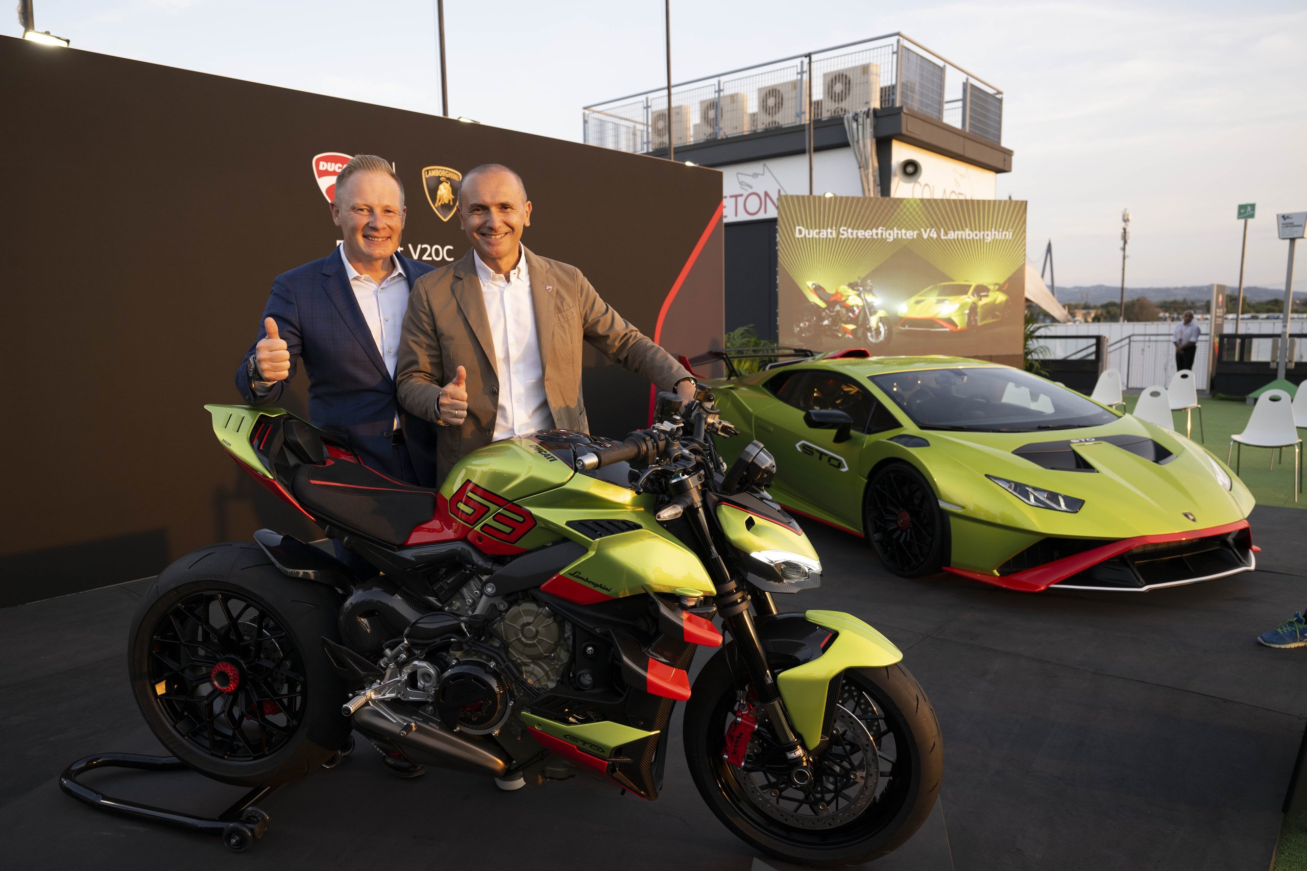 The Ducati Streetfighter V4 Lamborghini Puts The Huracán Sto In Your Garage On Two Wheels 3 Two men give thumbs up beside the ducati streetfighter v4 lamborghini with a matching huracán sto visible at an outdoor unveiling event