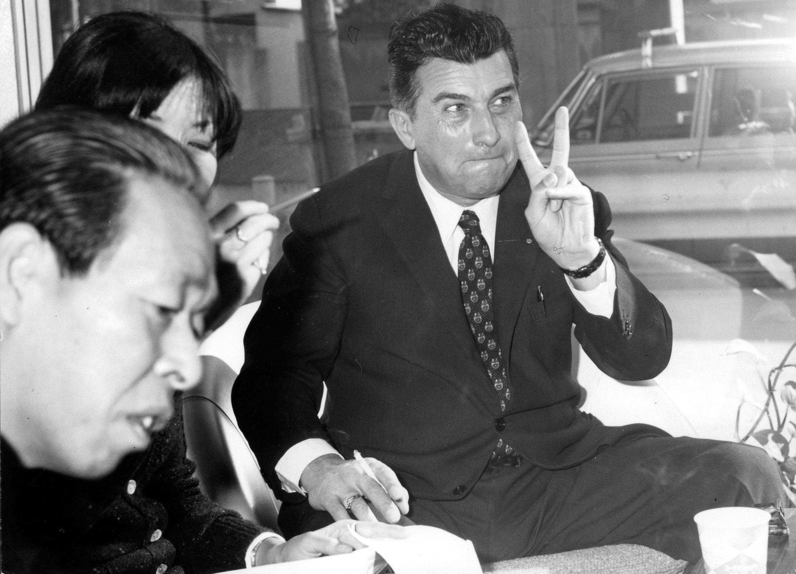 Ferruccio Lamborghini At 105: How A Stubborn Tractor Builder'S Grudge Created An Automotive Dynasty 7 Black and white image of ferruccio lamborghini making a peace sign gesture while seated at a table with others