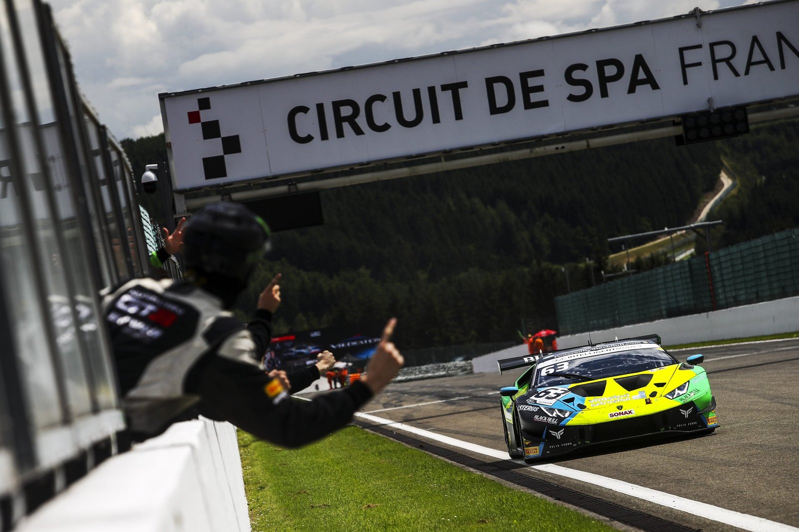 The #63 Lamborghini Huracán GT3 Evo in green and blue livery racing past a trackside official at Spa-Francorchamps
