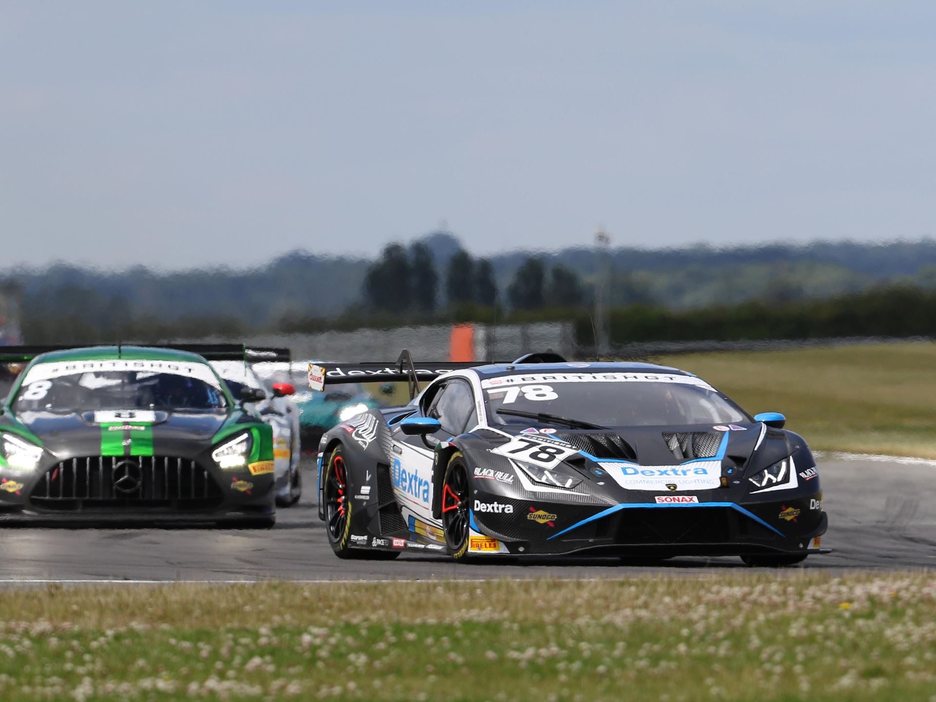 The number 78 lamborghini huracán gt3 evo2 leads a green mercedes-amg gt3 and other cars through a corner at snetterton