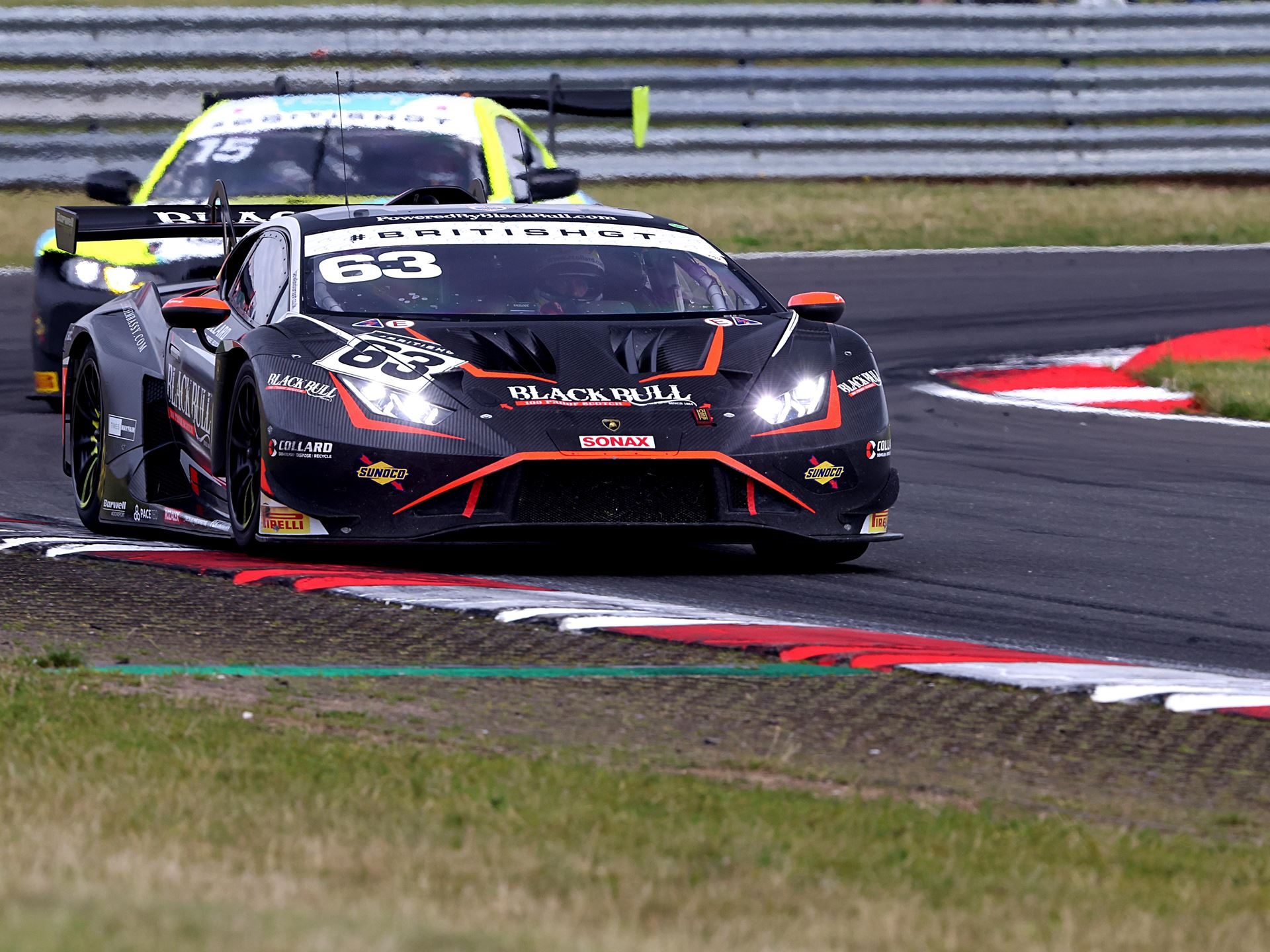 The black number 63 lamborghini huracán gt3 evo2 with orange accents navigates a corner at snetterton followed by a competitor
