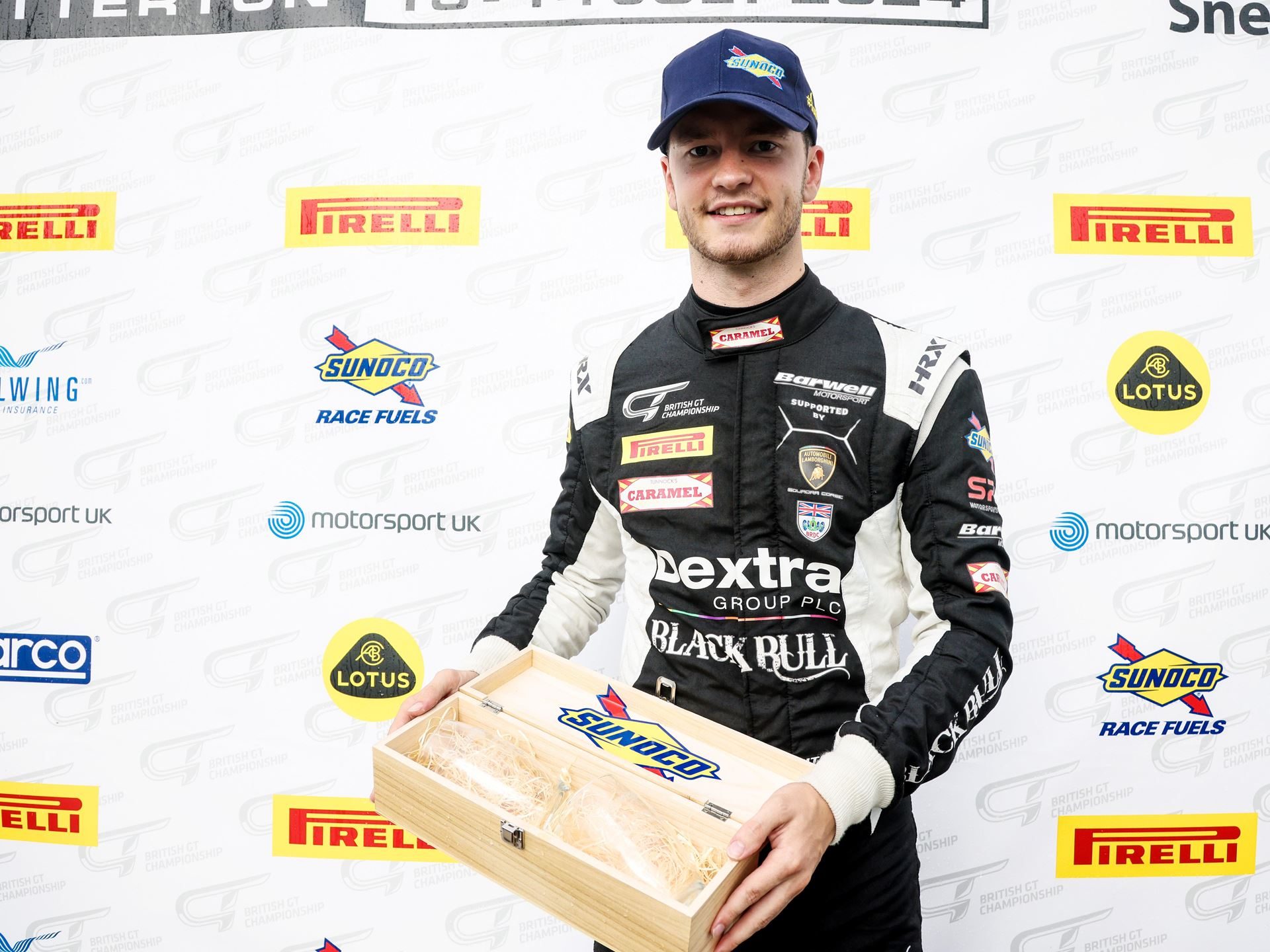 Sandy mitchell smiling while holding a wooden box trophy at a british gt championship event