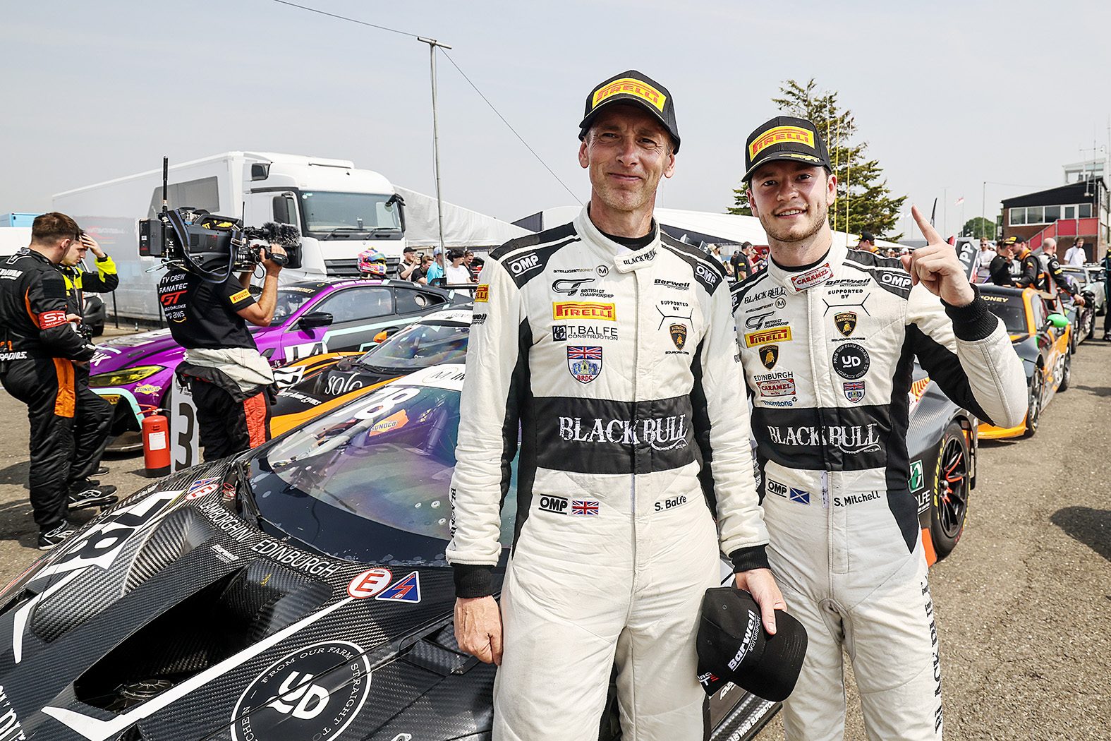 Two-Tenths Of A Second: How The Huracán Gt3 Evo2 Keeps Winning Before The Temerario Takes Over 5 Sandy mitchell and shaun balfe in white racing suits standing next to the black barwell motorsport huracán gt3 evo2 in the paddock