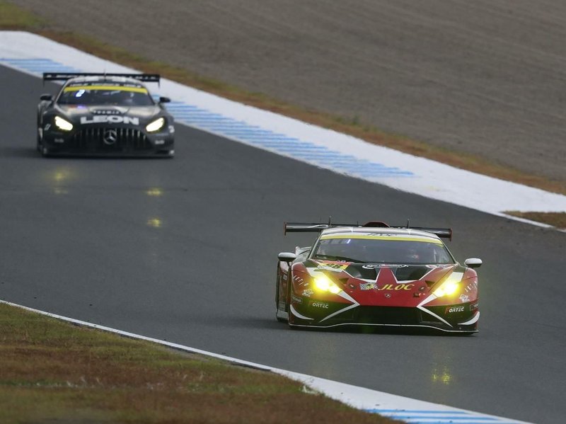 JLOC Lamborghini Huracán GT3 EVO2 in red and black livery leading a Mercedes-AMG GT3 on the Motegi circuit during the 2023 Super GT season finale