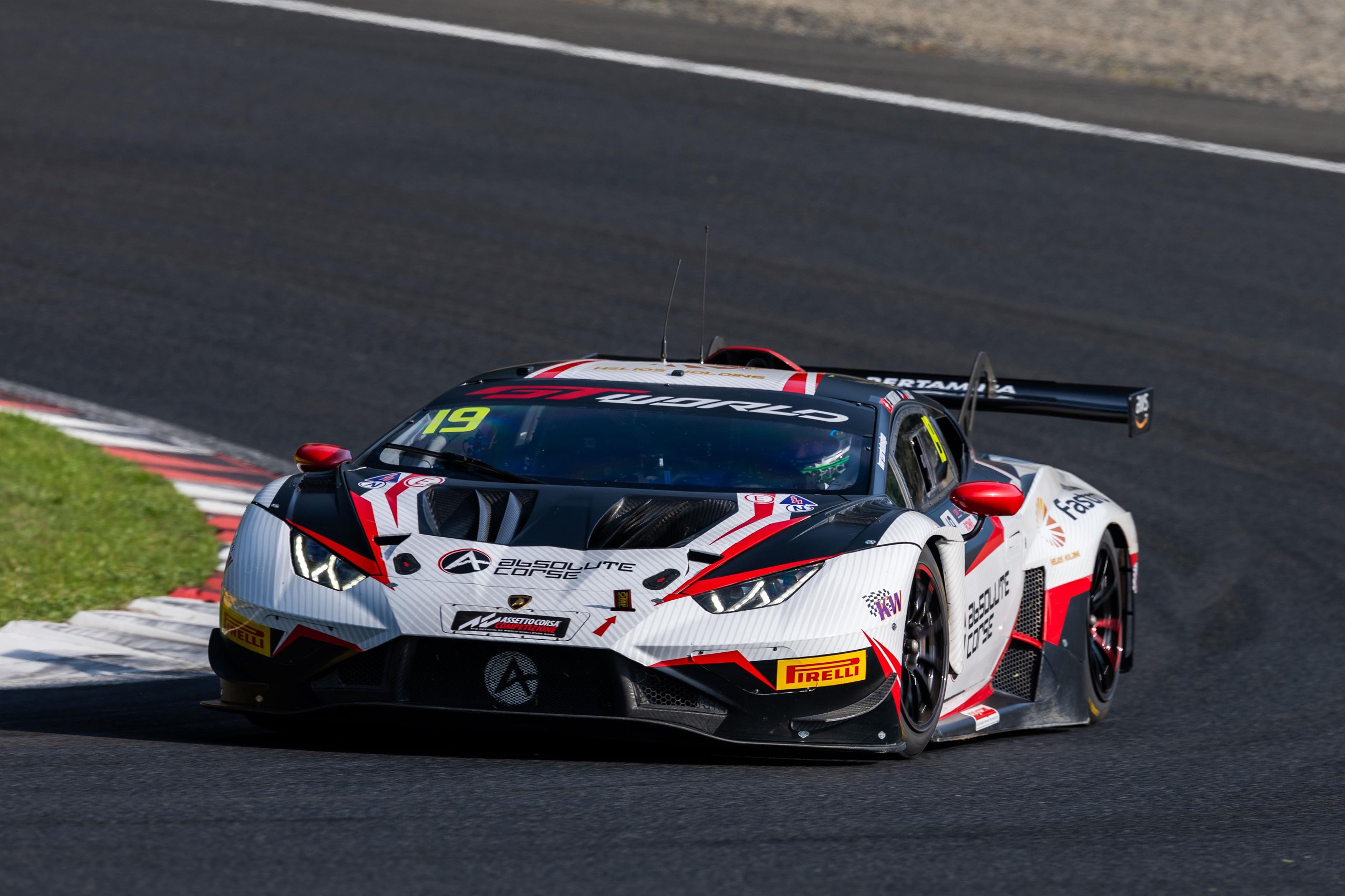 Lamborghini Huracán GT3 EVO race car navigating a turn on a sunlit race track, showing front splitter and wide stance