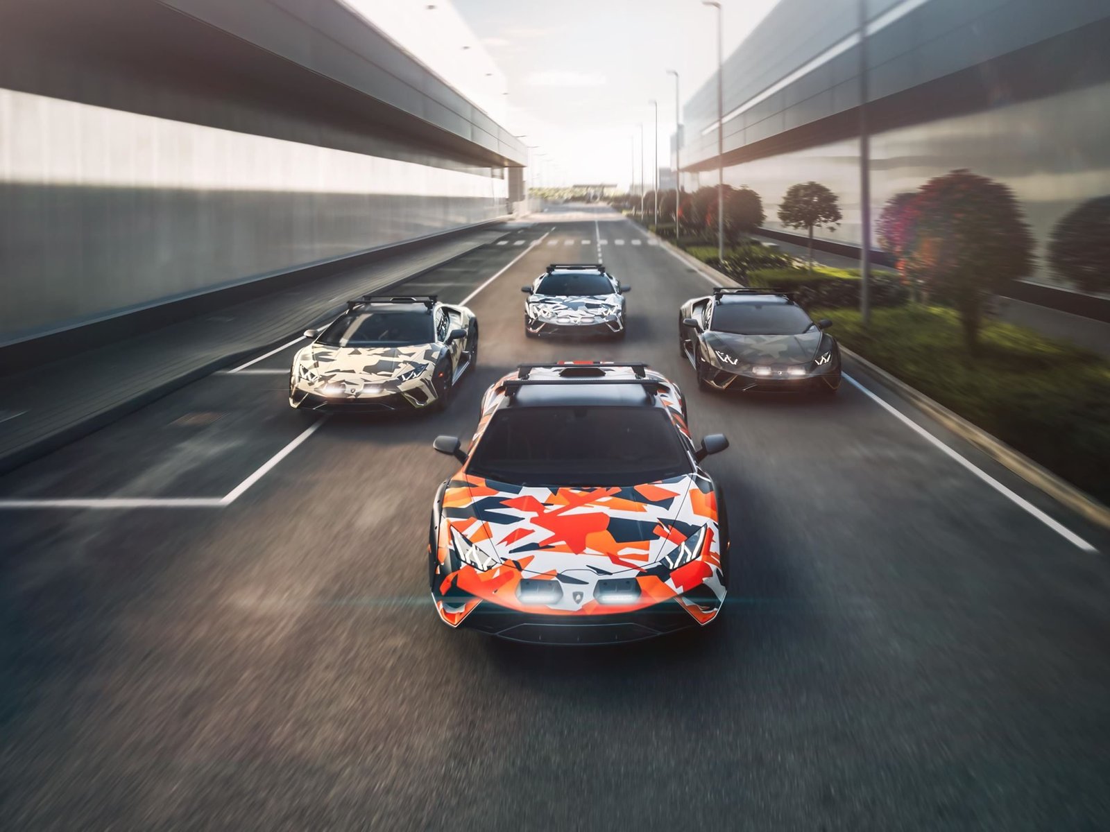 Four Lamborghini Huracán Sterrato All Terrain models in distinct camouflage liveries driving in formation on an urban road