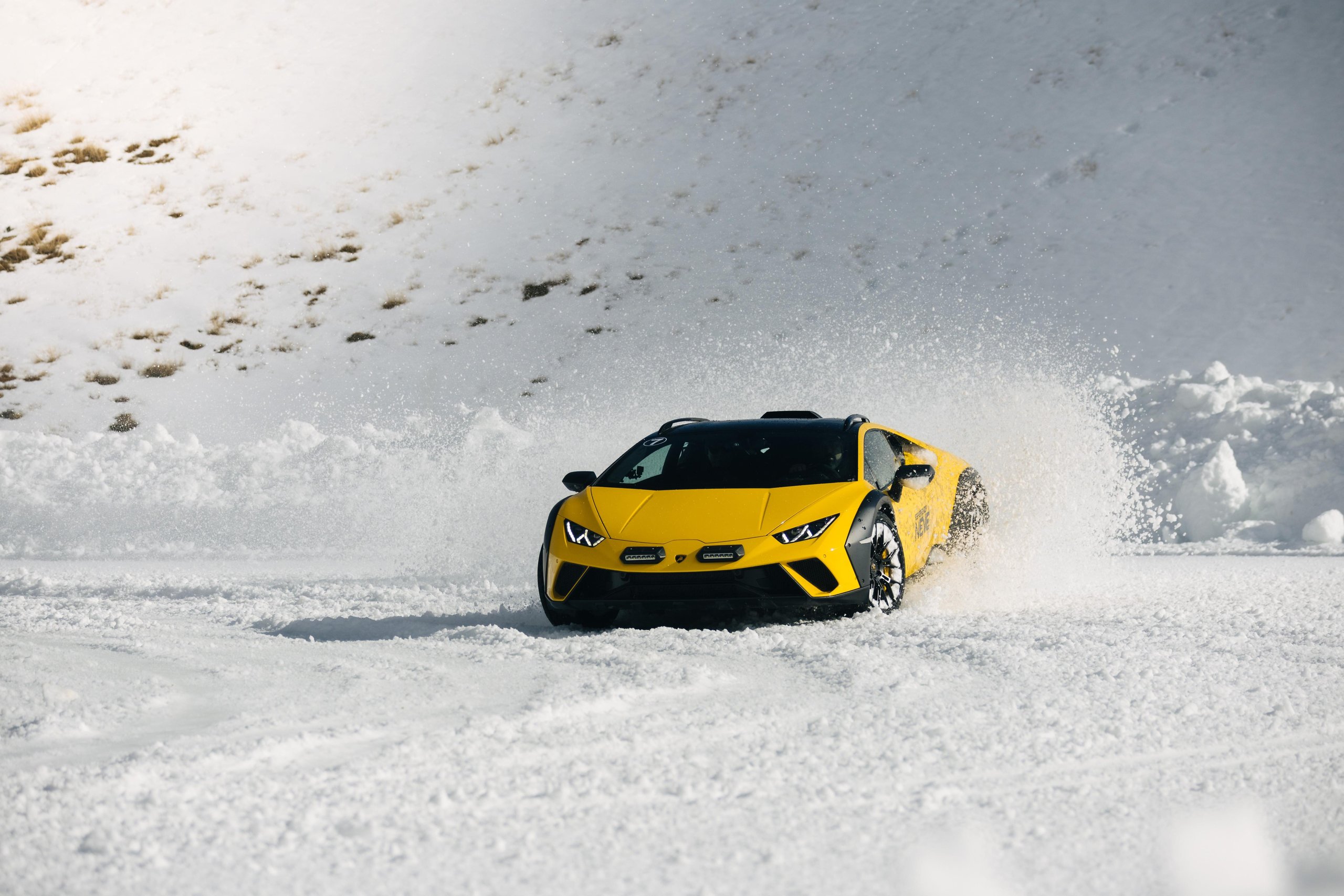 Yellow lamborghini huracán sterrato drifting through snow with raised suspension and roof rails visible