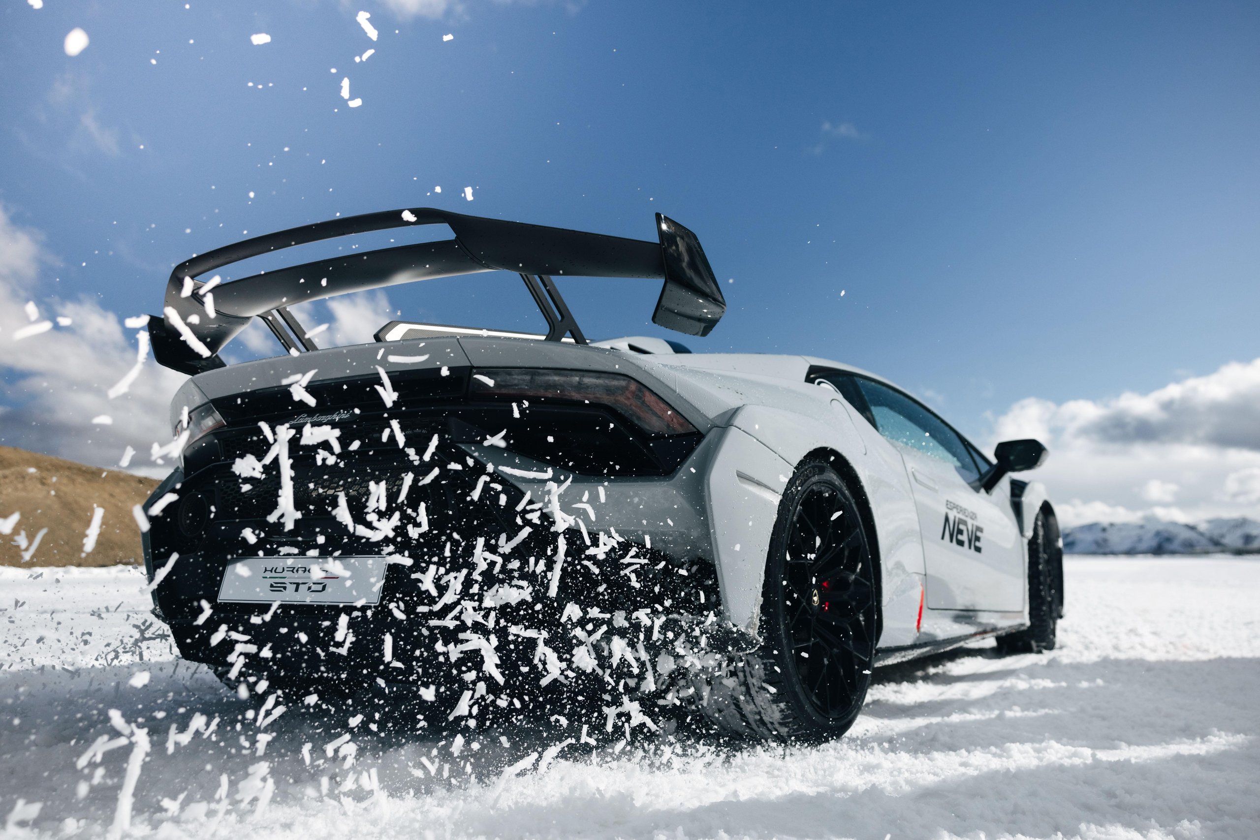 White lamborghini huracán sto drifting on snow with dramatic rear tire spray under blue sky