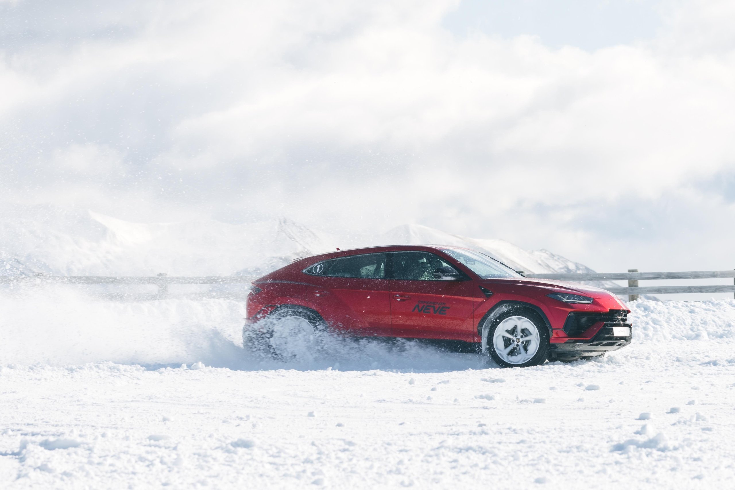 Red lamborghini urus driving through deep snow with mountain landscape in background