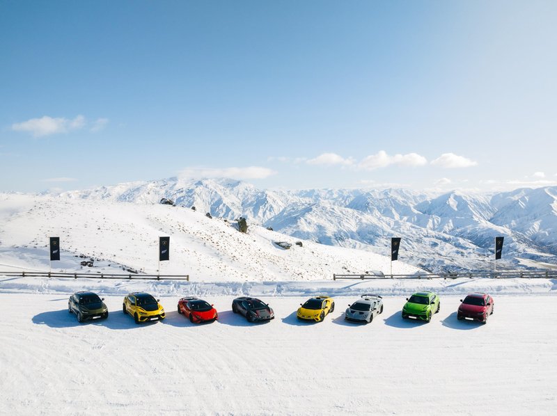 Multiple Lamborghini models lined up on a snow-covered plain in Queenstown, New Zealand, with a mountain range under clear blue sky
