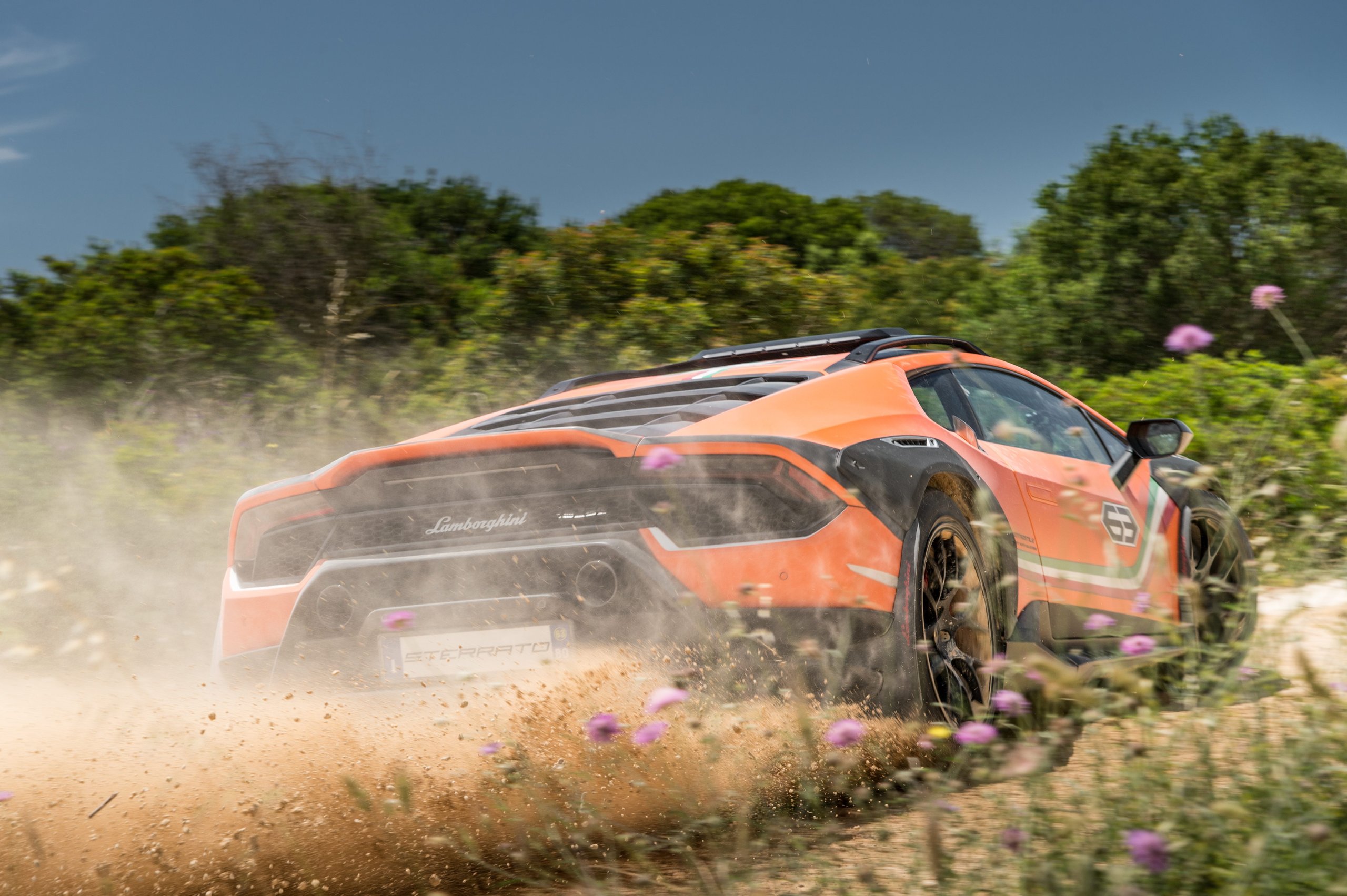 How A Dusty Dinner Conversation And Chassis #53 Gave Birth To The Huracán Sterrato 7 Rear view of the orange huracán sterrato concept speeding away on an unpaved road with dust billowing behind it, showing wide fender flares and dual exhaust