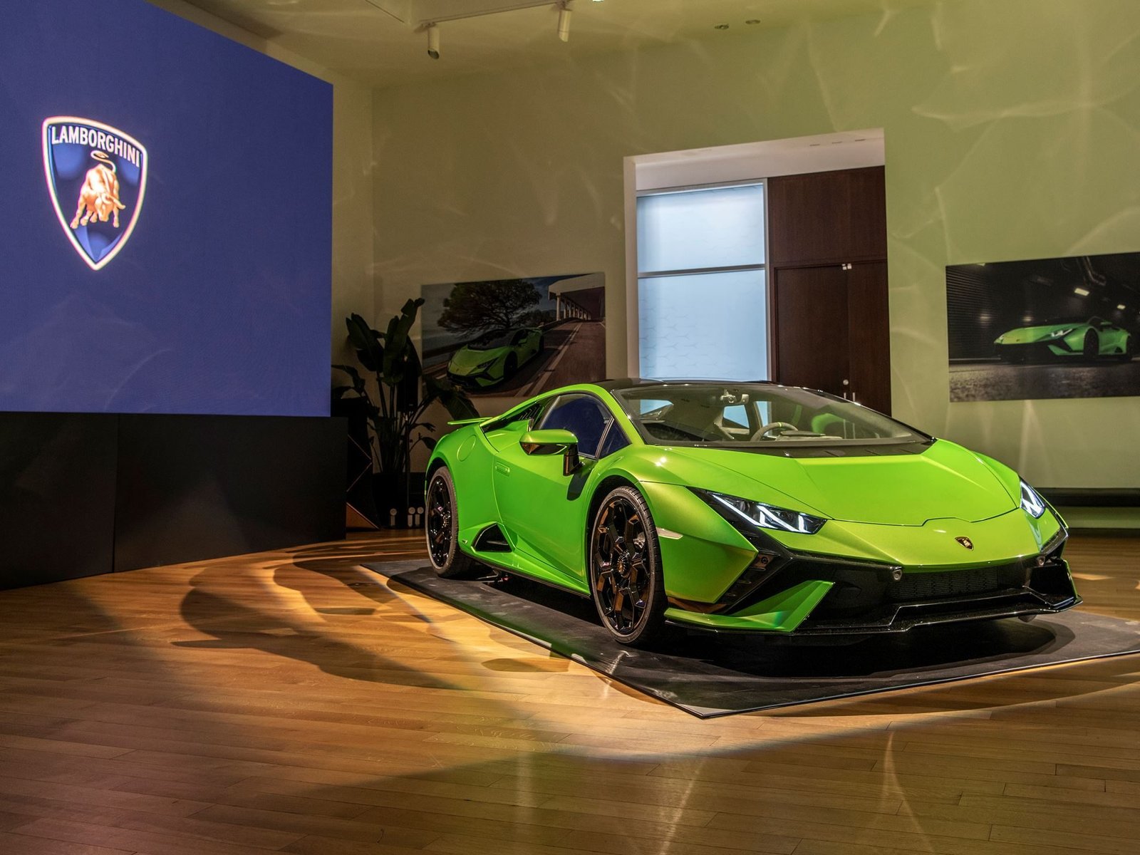 Vibrant green Lamborghini Huracán Tecnica on a black platform at the Lamborghini Lounge NYC event with the Lamborghini logo displayed on screen behind it