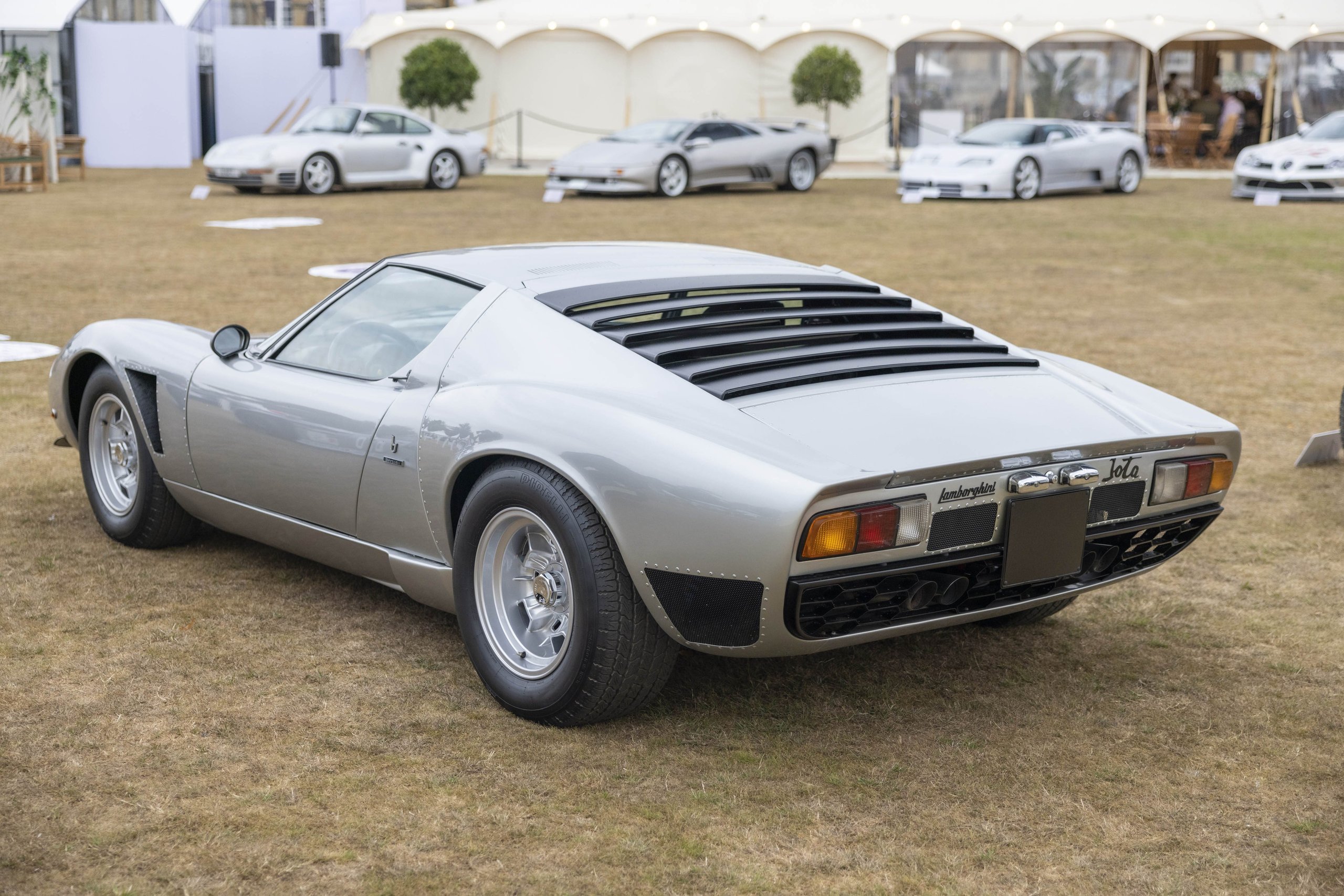 Lamborghini Paired The Huracán Tecnica With Its Rarest Classics At Salon Privé, And The Subtext Was Deliberate 5 Rear three-quarter view of the silver 1973 lamborghini miura p400 svj showing rear louvers and classic taillights on the salon privé lawn