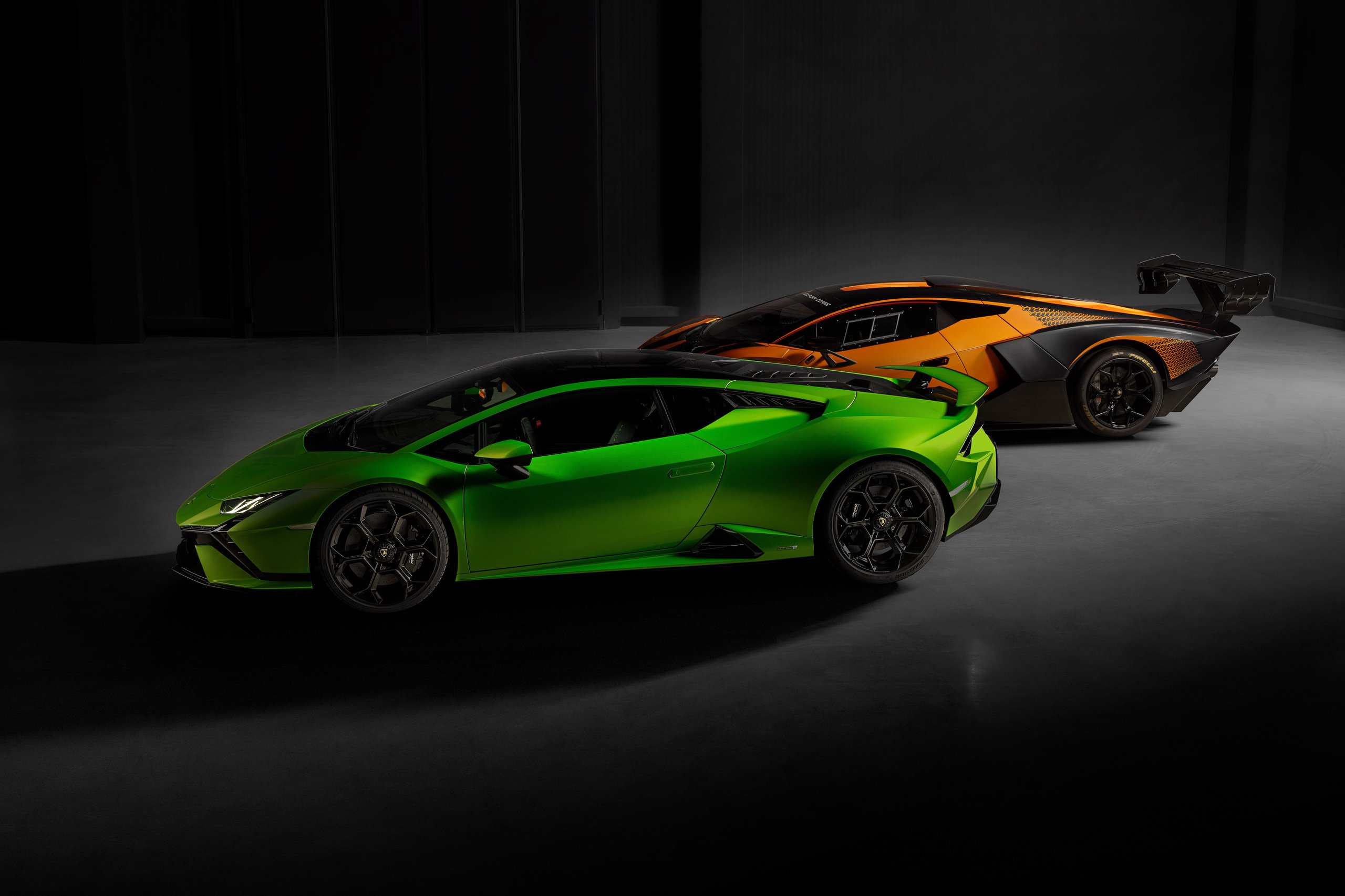 Huracán Tecnica: Lamborghini'S Case That The Best V10 Splits The Difference 9 Two lamborghini huracán models side by side in a dark studio: the tecnica in verde mantis green and the sto in orange, showing contrasting aerodynamic packages and rear spoiler designs