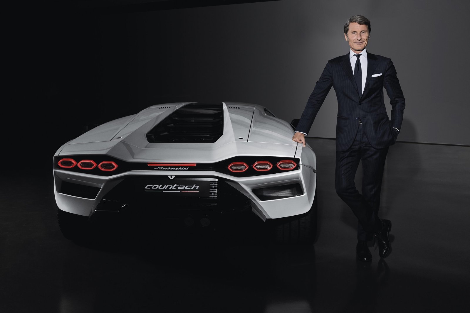 Stephan Winkelmann, CEO of Automobili Lamborghini, stands beside a white Lamborghini Countach LPI 800-4 in a studio setting