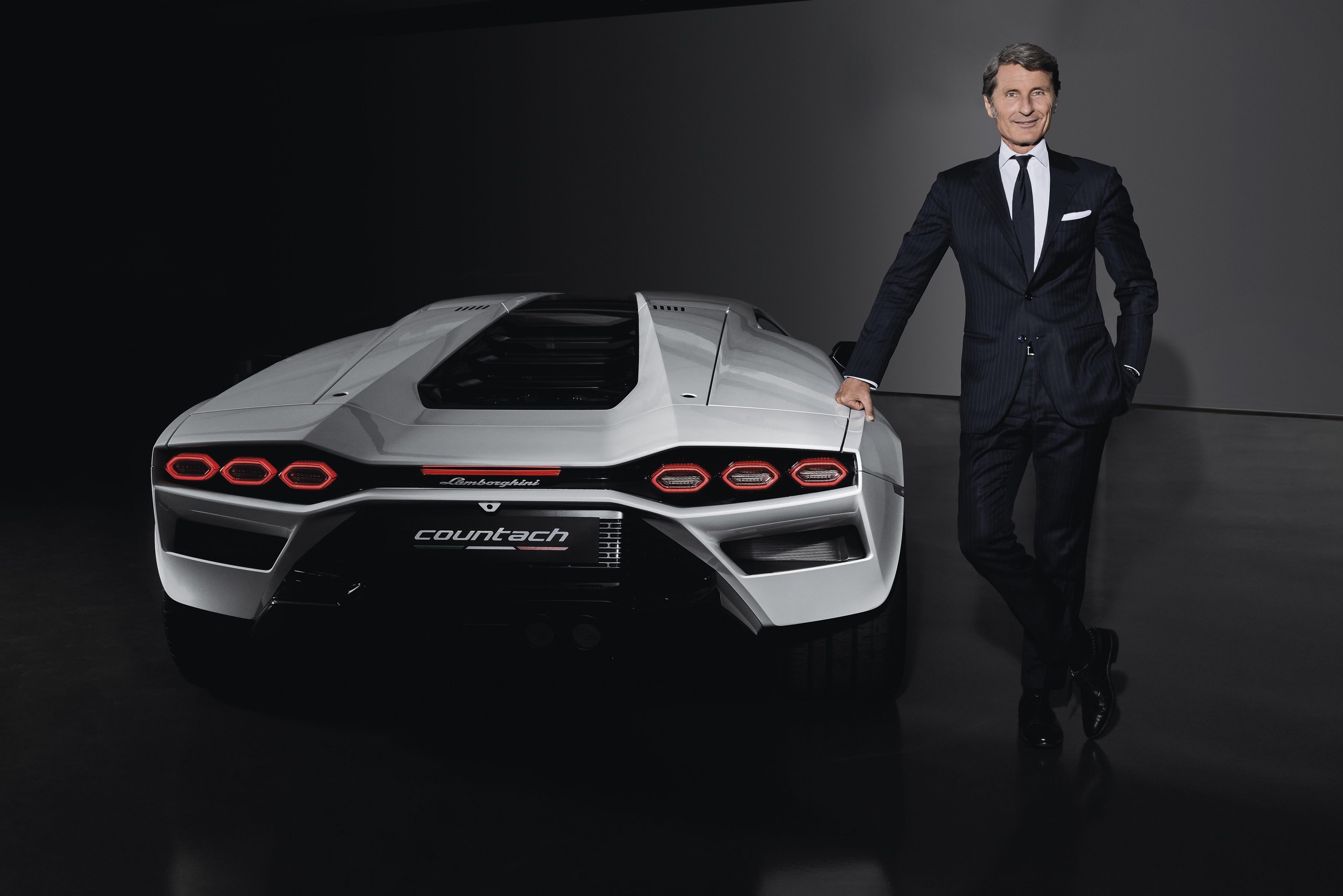 Stephan winkelmann, ceo of automobili lamborghini, stands beside a white lamborghini countach lpi 800-4 in a studio setting