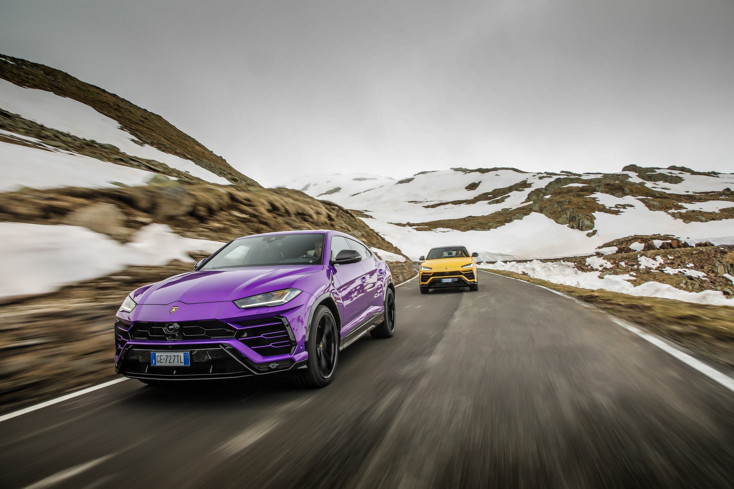 How 8,405 Cars And One Suv Are Funding Lamborghini'S €1.5 Billion Bet On Electrification 5 Two lamborghini urus suvs, one purple and one yellow, driving on a snowy mountain road