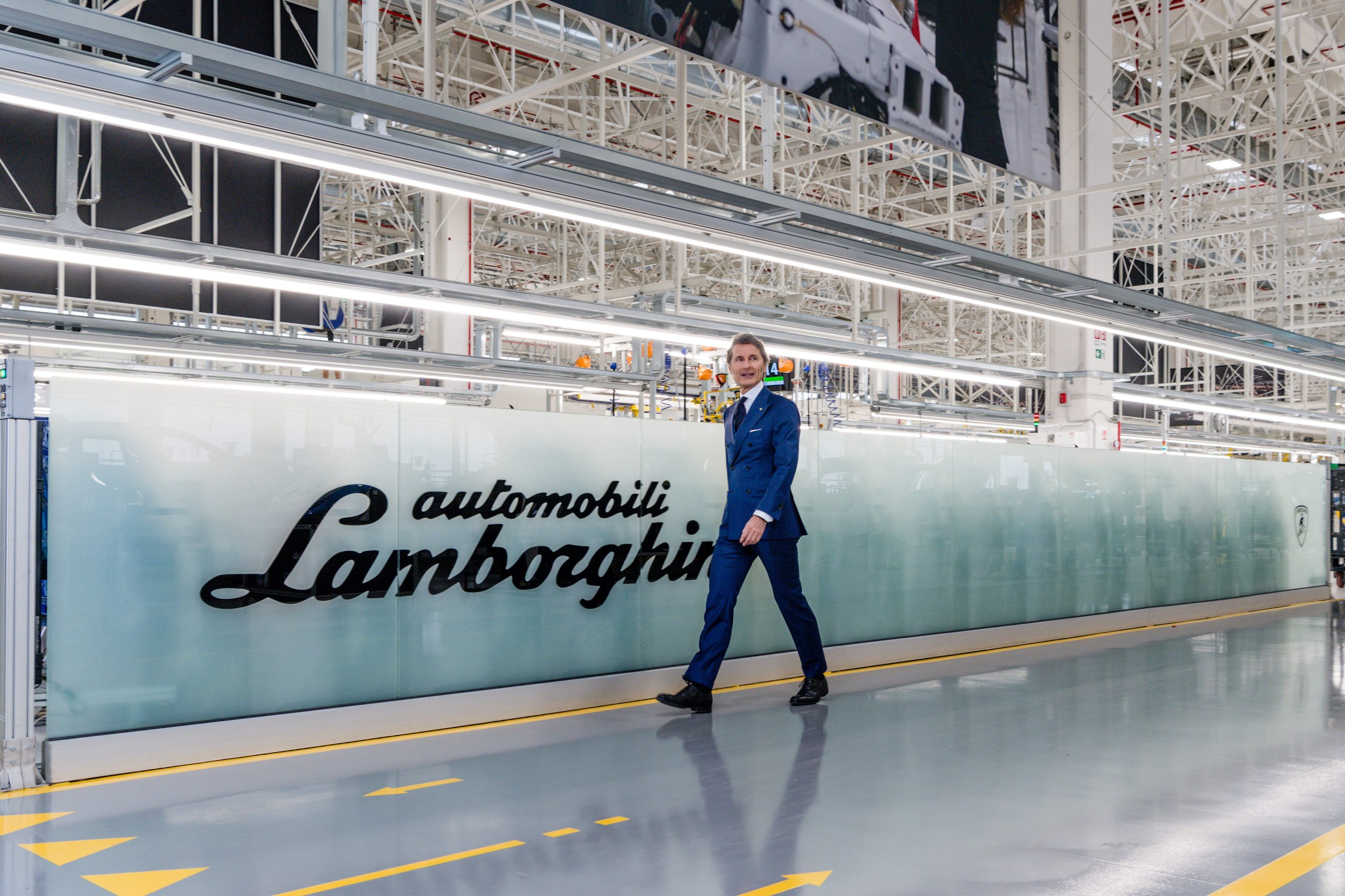How 8,405 Cars And One Suv Are Funding Lamborghini'S €1.5 Billion Bet On Electrification 7 Stephan winkelmann walking across the lamborghini factory floor with the automobili lamborghini logo on the wall behind him