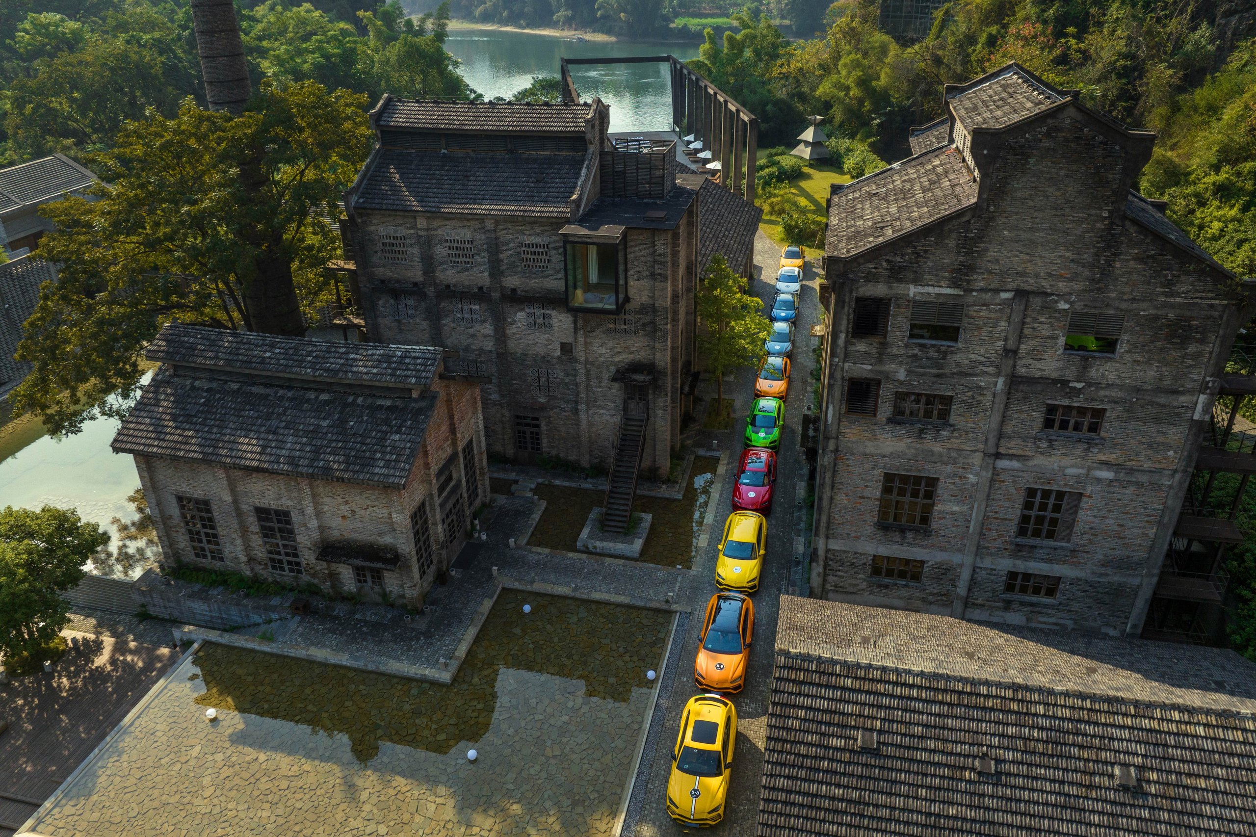 Aerial view of colorful lamborghini urus suvs lined up between historic brick buildings in a european village