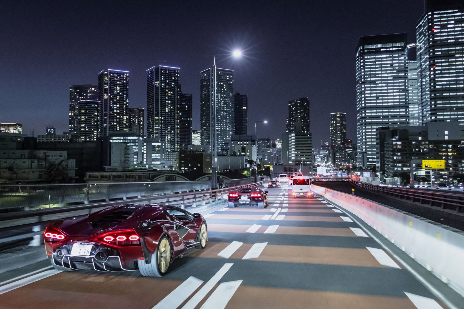 Red Lamborghini Sián FKP 37 driving on a highway at night with illuminated city skyscrapers in the background