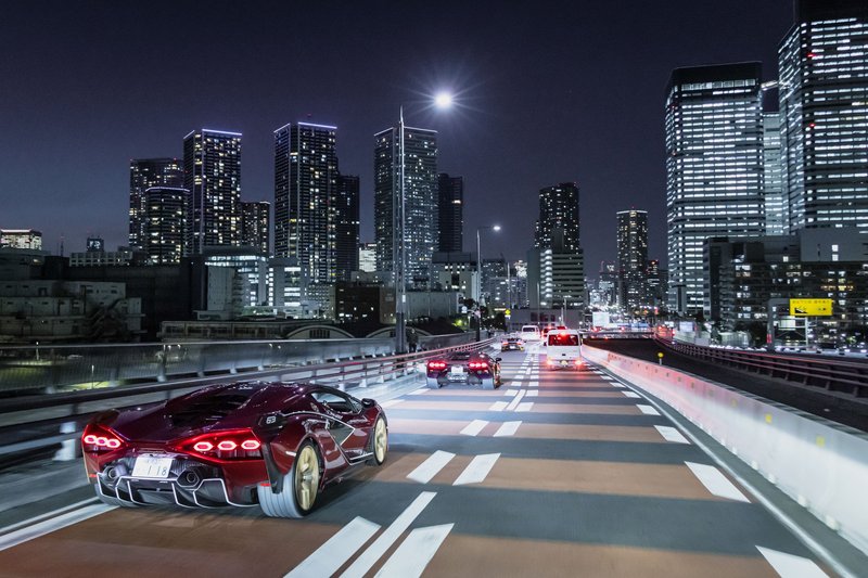 Red Lamborghini Sián FKP 37 driving on a highway at night with illuminated city skyscrapers in the background