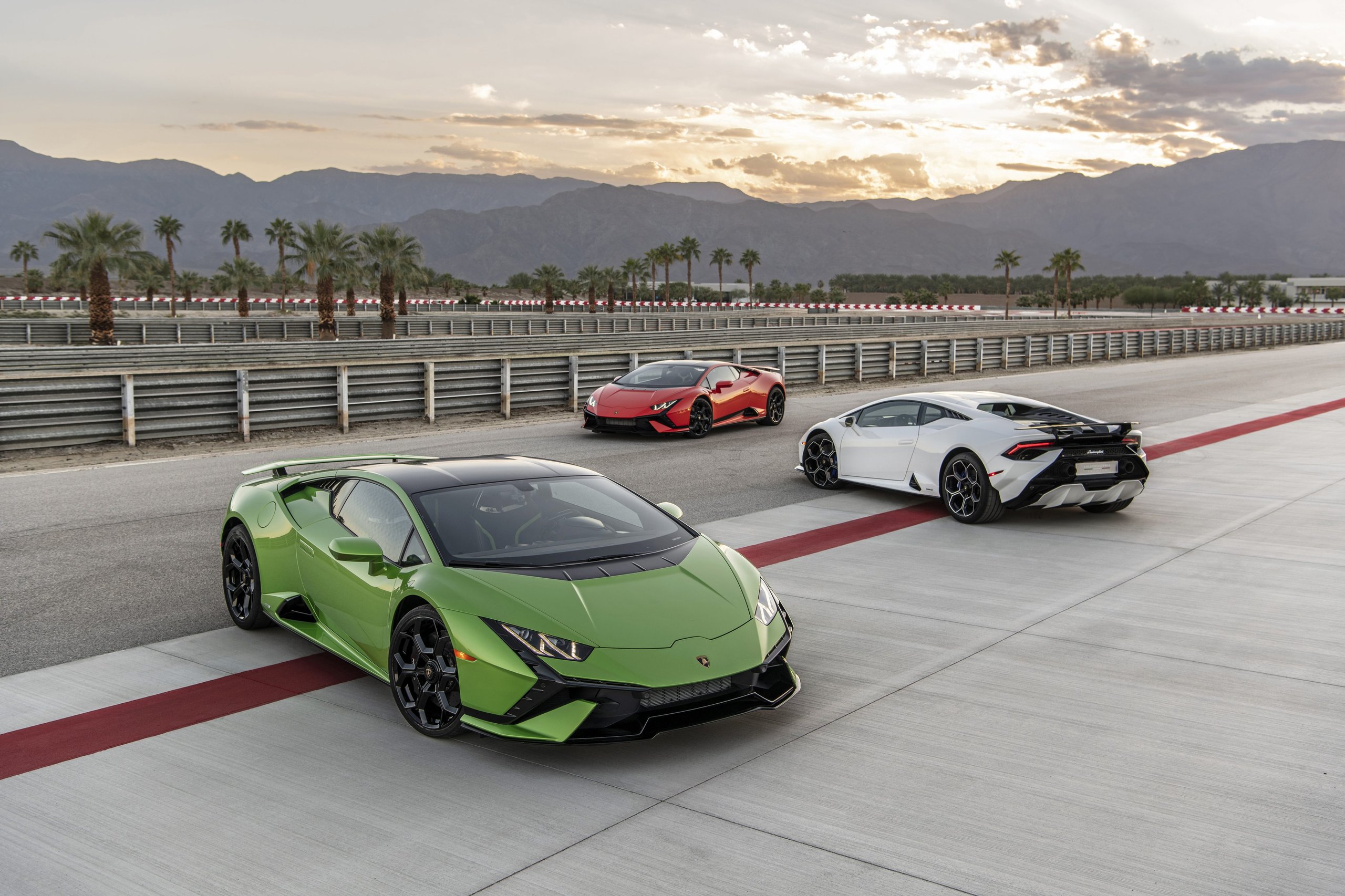 Three lamborghini huracán variants parked on a race track at sunset with palm trees and mountains in the background