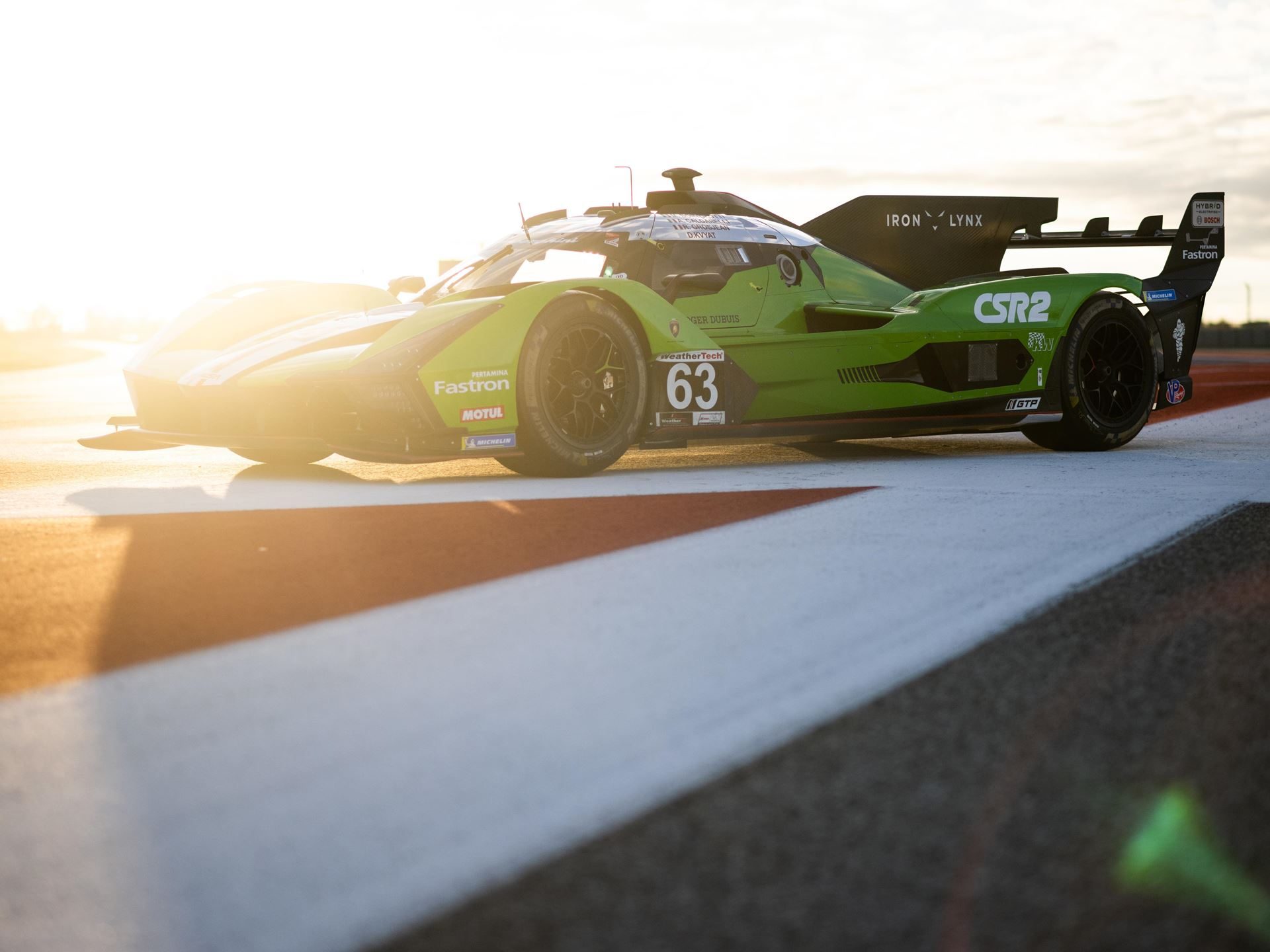 Green lamborghini sc63 hybrid race car on a racetrack at sunrise