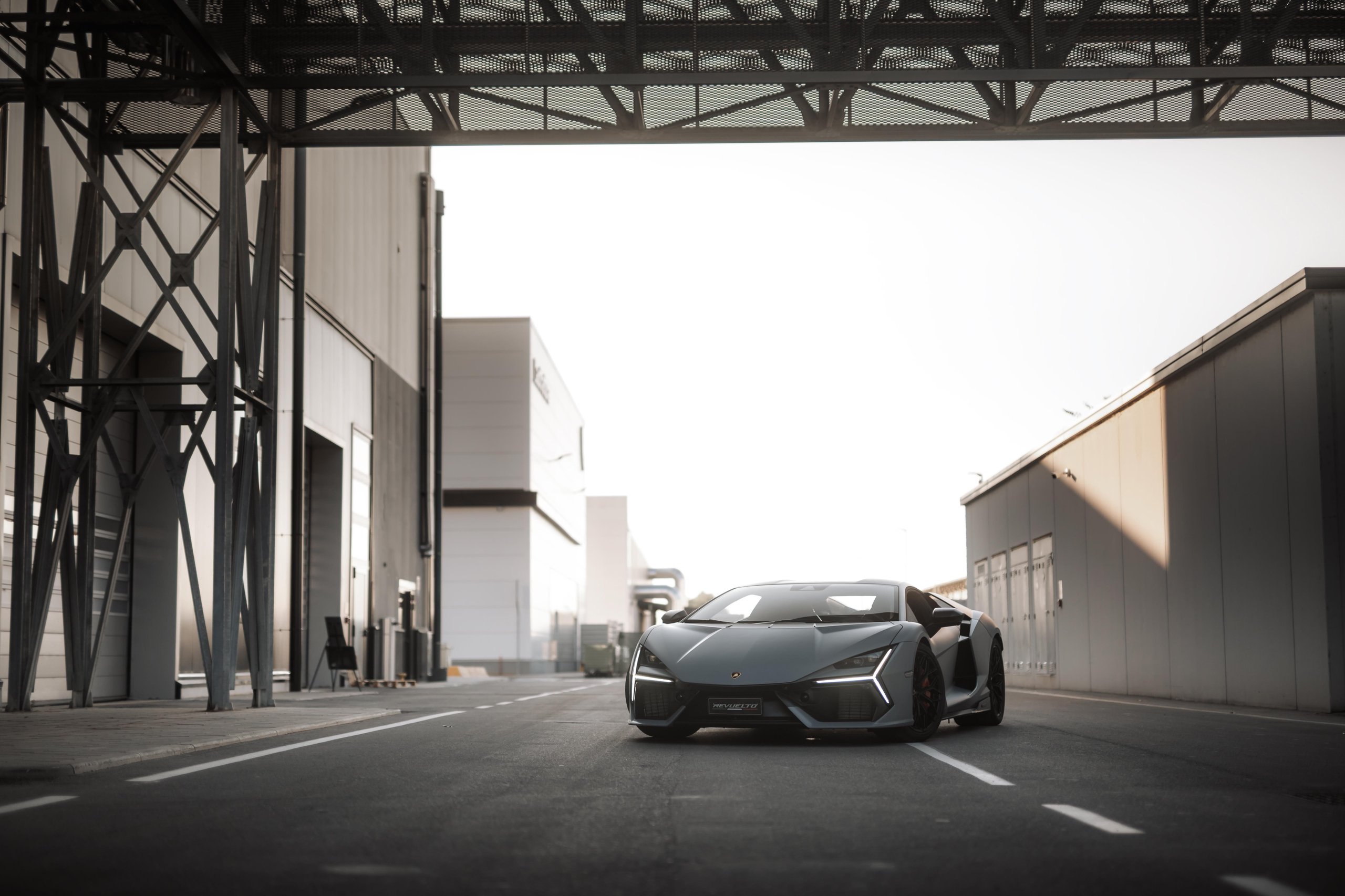 Grey lamborghini revuelto parked on an industrial road between factory buildings