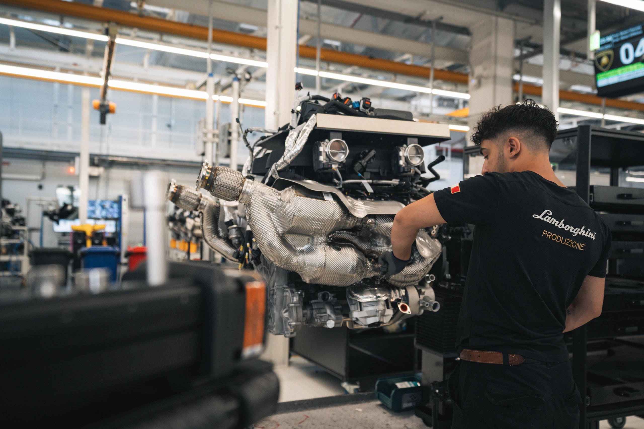 A lamborghini production worker in a lamborghini produzione shirt assembling a complex engine in a brightly lit factory