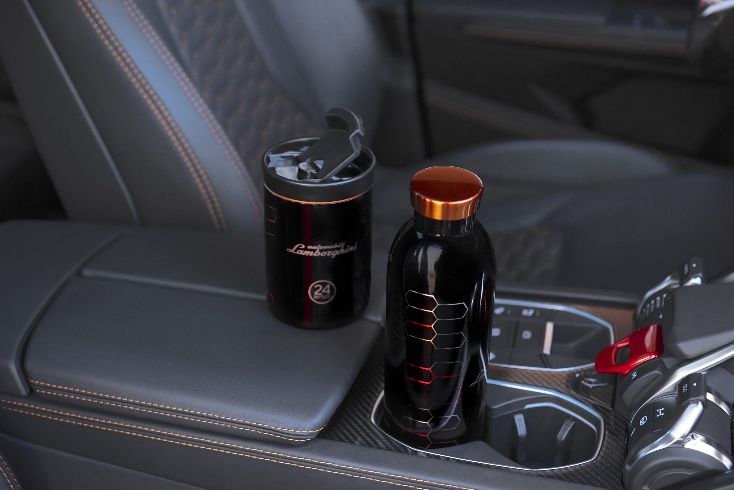 Lamborghini'S Lifestyle Gambit: How Thermal Bottles And Kids' Fashion Aim To Build The Next Generation Of Owners 3 Two black lamborghini branded thermal bottles by 24bottles sitting in the cup holders of a lamborghini urus interior with orange contrast stitching