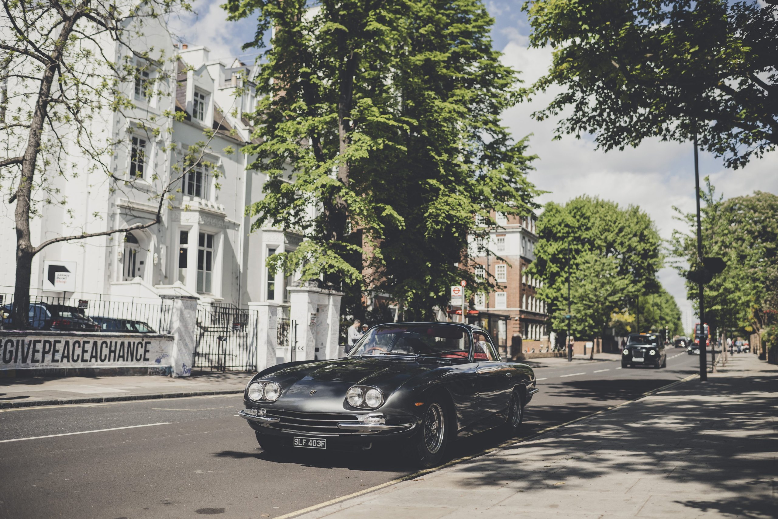 Lamborghini Celebrates The Beatles' Legacy With A 400 Gt 2+2 London Tour 3 Dark green lamborghini 400 gt 2+2 on a london street with 'give peace a chance' graffiti visible in the background