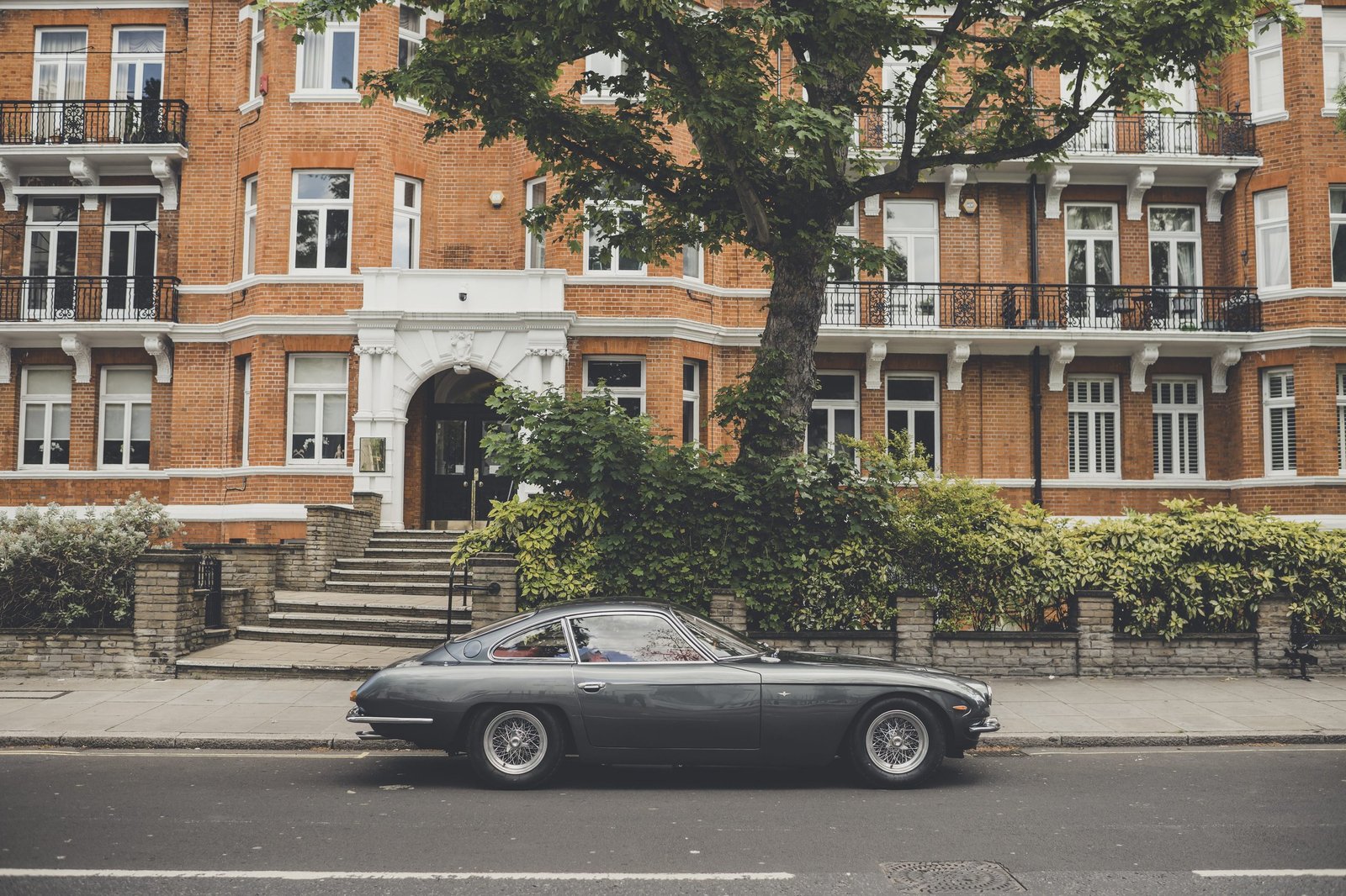 Dark green Lamborghini 400 GT 2+2 parked in front of a classic London brick building with white trim and balconies