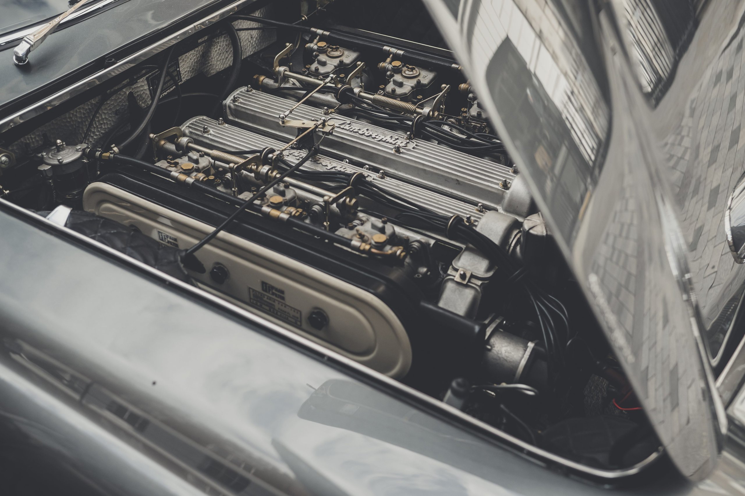 Lamborghini Celebrates The Beatles' Legacy With A 400 Gt 2+2 London Tour 7 Top-down close-up of the lamborghini 400 gt 2+2 v12 engine bay showing carburetors, polished valve covers, and lamborghini script