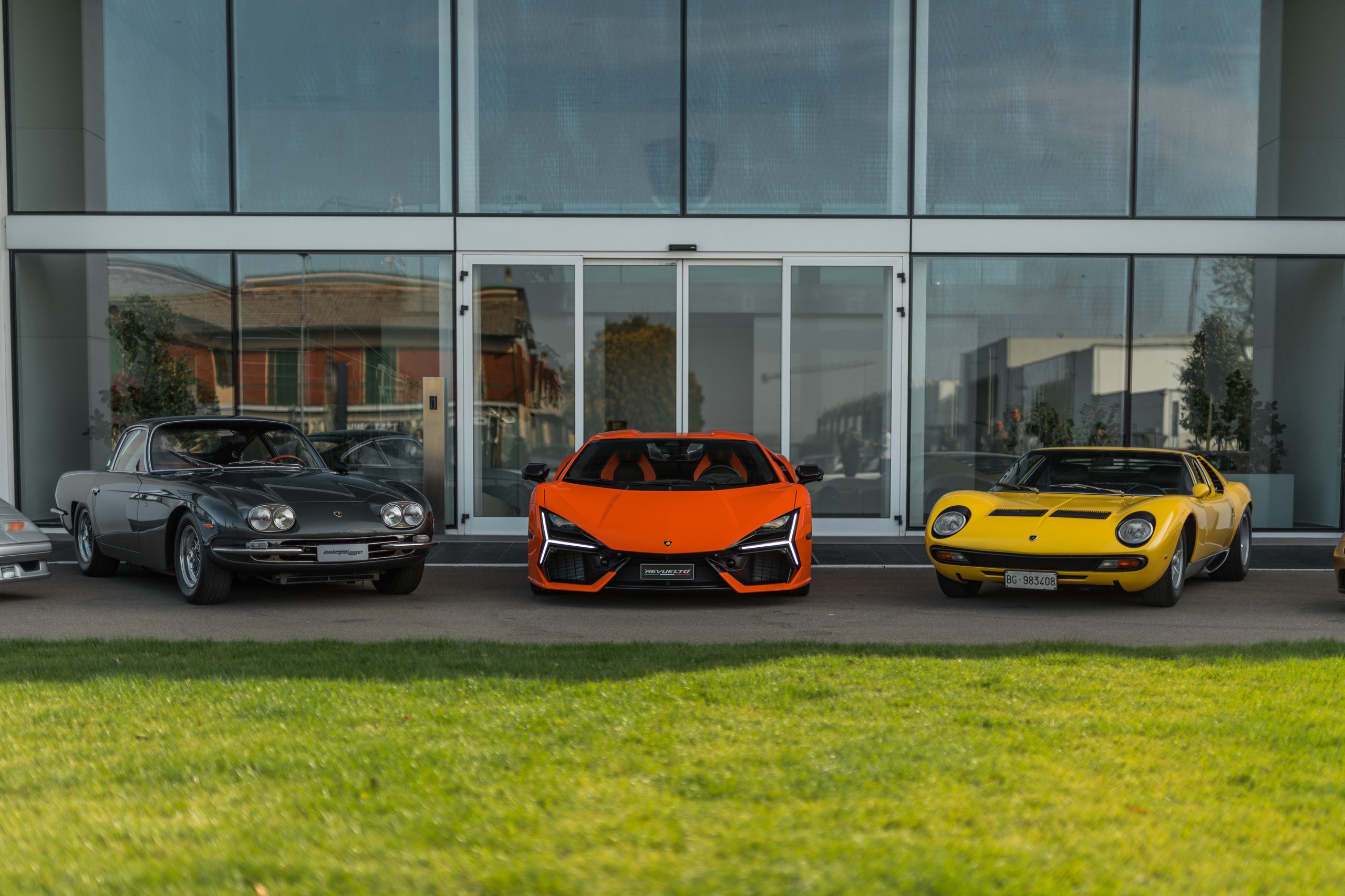 Lamborghini At 60: Global Owner Gatherings And Two 60-Unit Huracans Mark Six Decades Of Defiance 7 Three lamborghini models spanning decades, a grey 400 gt, orange sian, and yellow miura, parked together in front of a modern glass building