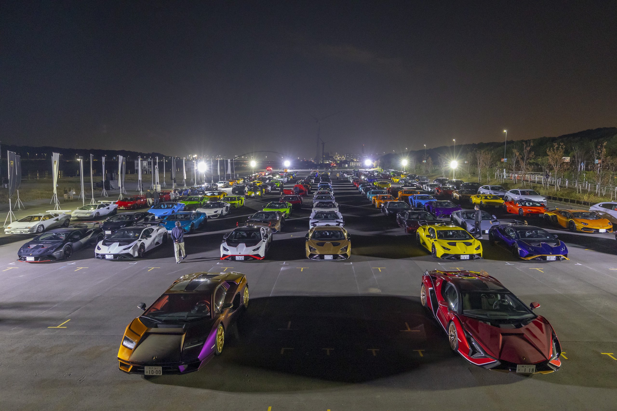 A vast array of colorful modern lamborghini supercars parked in rows at night, illuminated by artificial lights