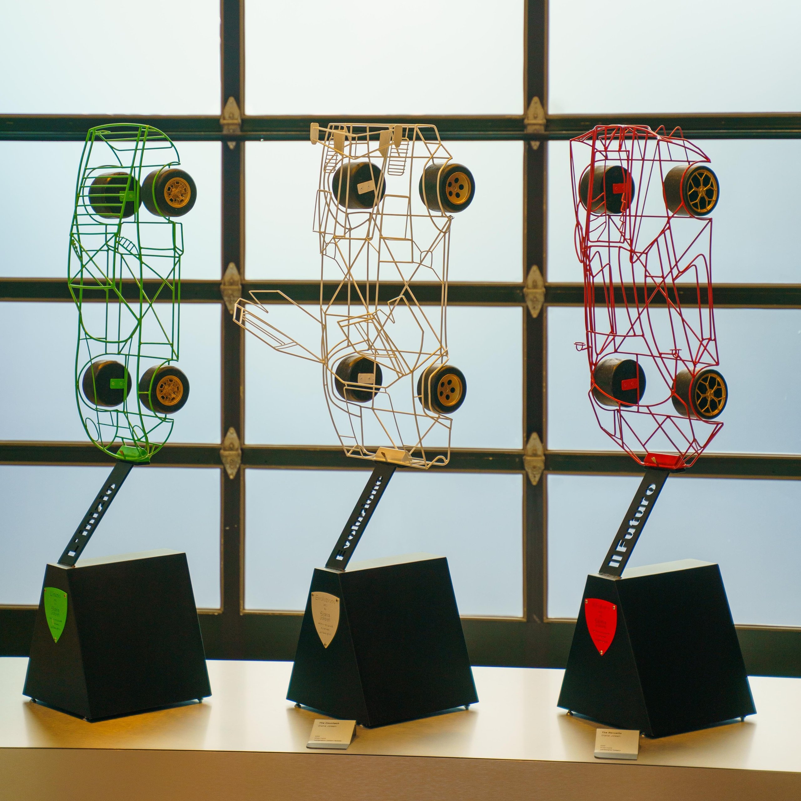 Why Lamborghini Opened Its Private Nyc Lounge To The Public For The First Time 9 Three wireframe car chassis sculptures in green gold and red on pedestals labeled ieri oggi il futuro