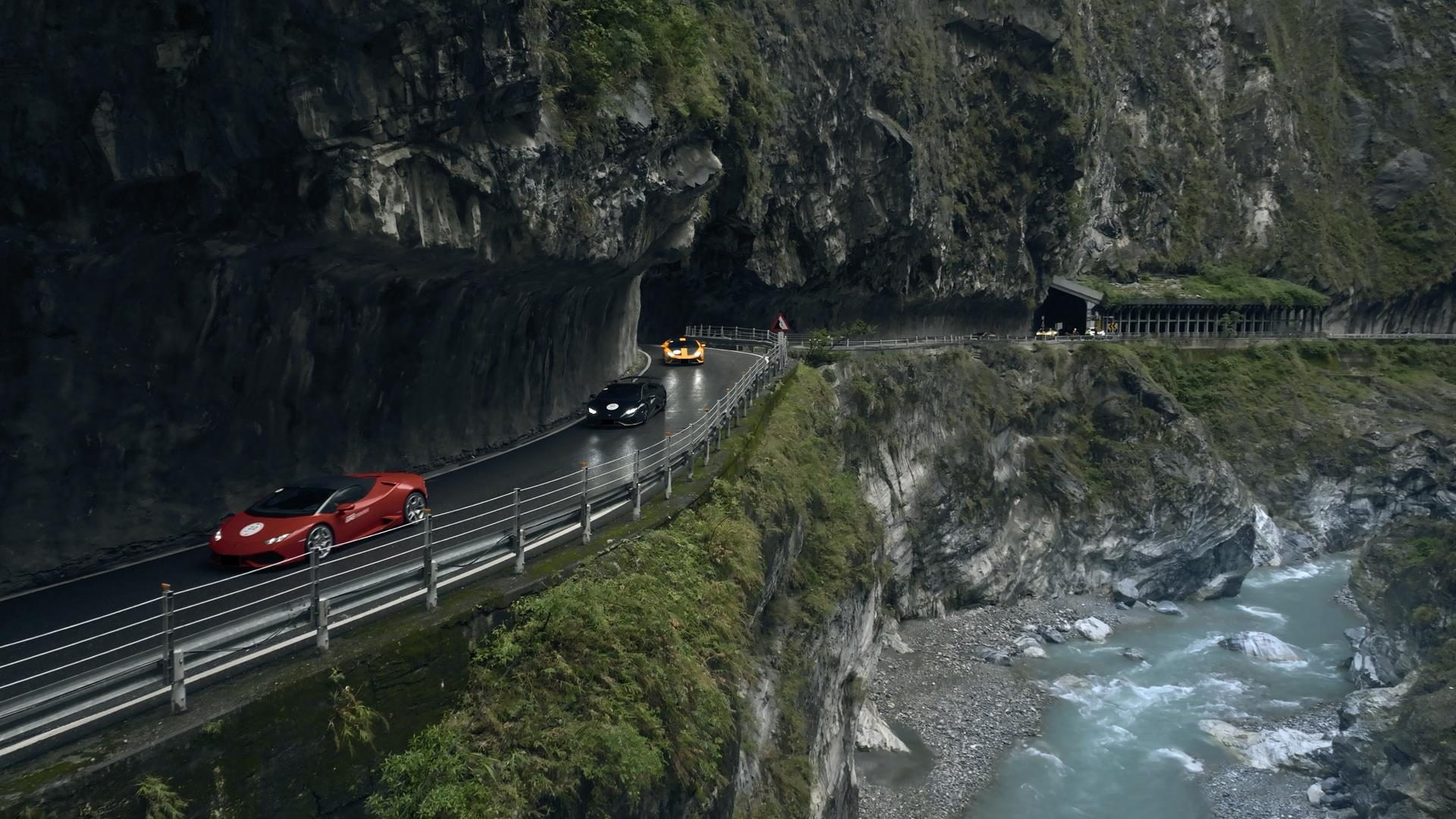 Seventy Lamborghinis, One Kinetic Sculpture, And Taiwan'S Eastern Coast: Inside The 60Th Anniversary Esperienza Giro 7 A red lamborghini huracán leads a convoy along a winding road carved into a steep rocky mountain face with a river below