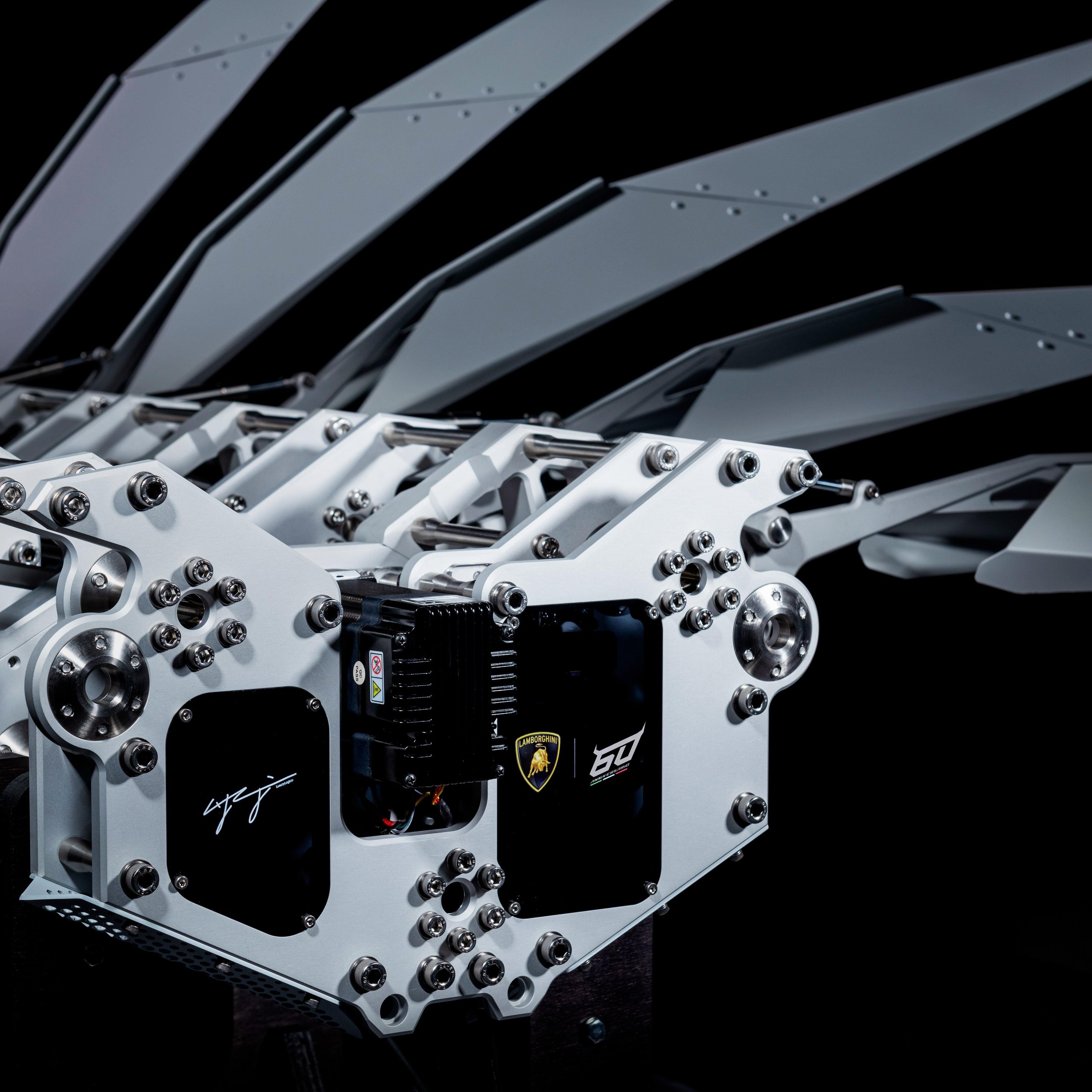 Close-up of the LL60 kinetic sculpture's mechanical core showing precision gears, bolts, and the Lamborghini 60th-anniversary logo