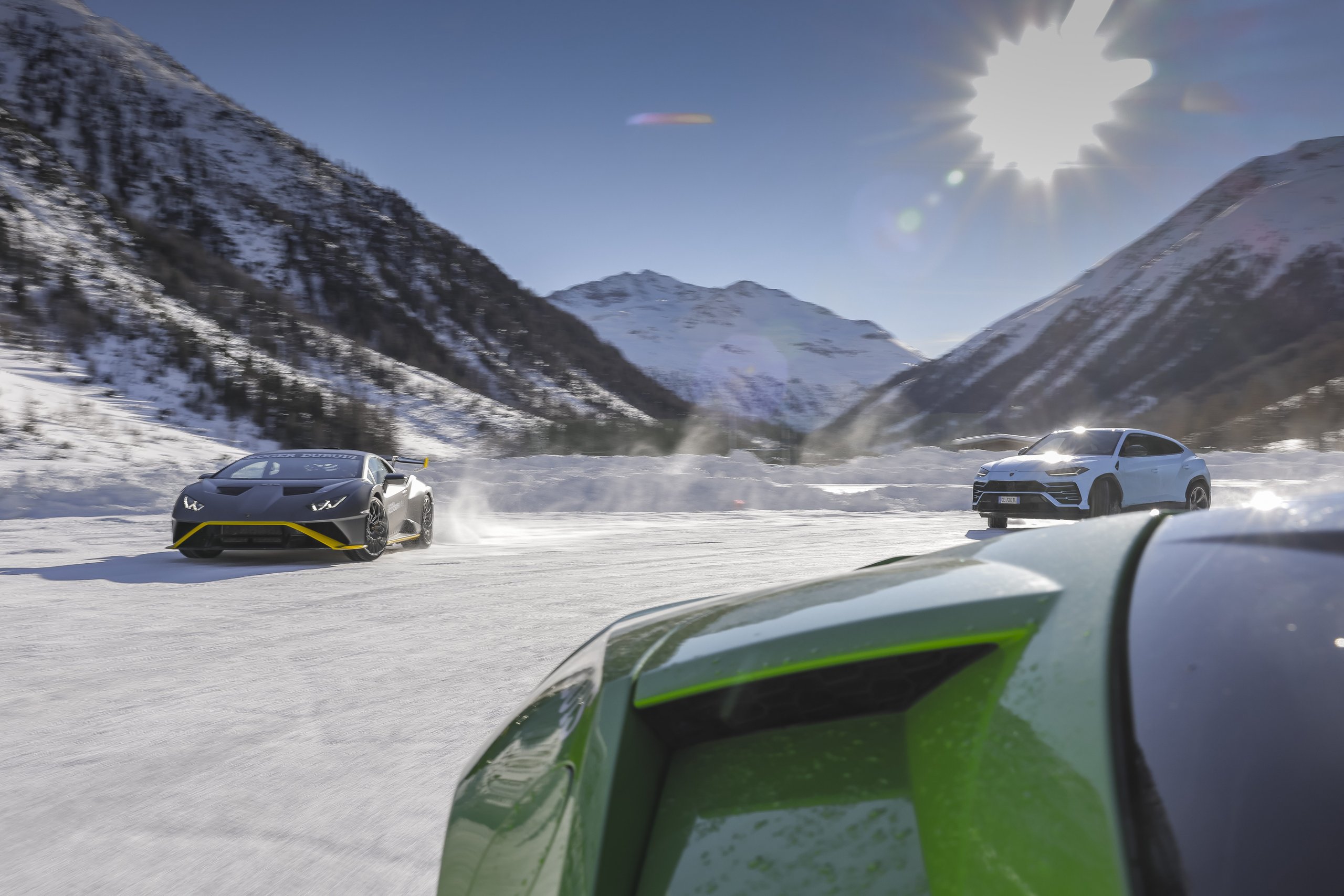 Accademia Neve 2022: What Lamborghini'S Ice Driving Program Actually Teaches Owners About Their Cars 11 Grey lamborghini huracán and light blue urus driving together on a snowy track with mountains in background under bright sun at accademia neve 2022