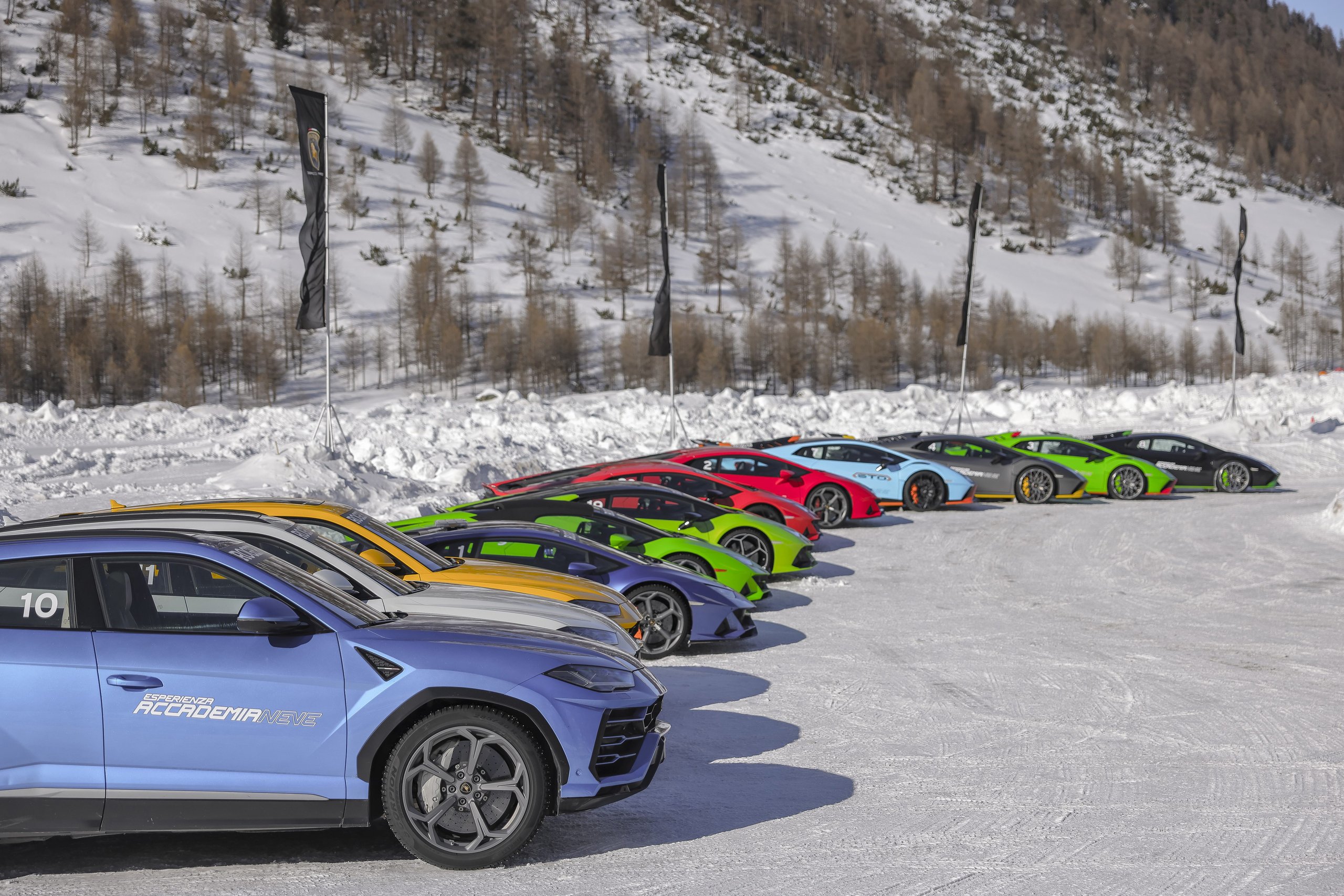 Accademia Neve 2022: What Lamborghini'S Ice Driving Program Actually Teaches Owners About Their Cars 3 Long line of colorful lamborghini urus and huracán models parked on snow-covered surface at accademia neve 2022 with snow-laden trees and mountains